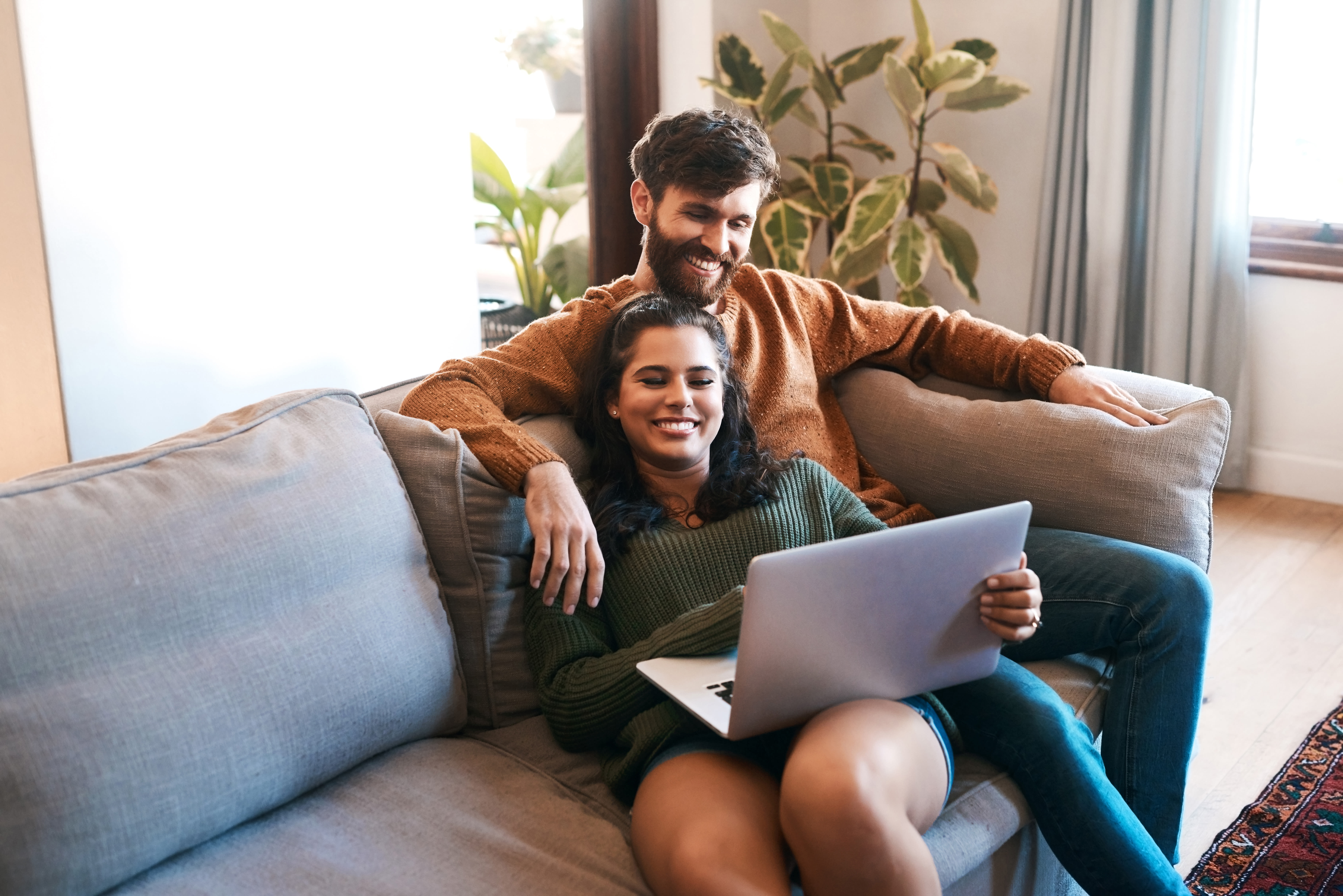 Happy young couple sitting on sofa using laptop together at Sutter Green Apartments in Sacramento, California