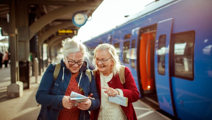 Elderly women looking at a map and smiling at a train station.