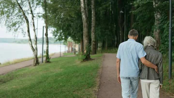 Two elderly adults walking down a path with their arms around each other