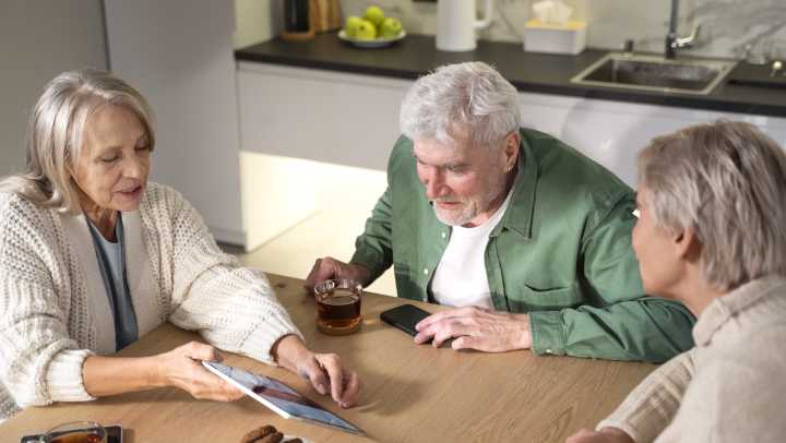 Group of elderly adults giving around a table with tea and cookies