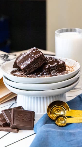 Chocolate brownies with chocolate syrup and powdered sugar on top, adorned with chocolate squares, gold measuring spoons and a glass of milk