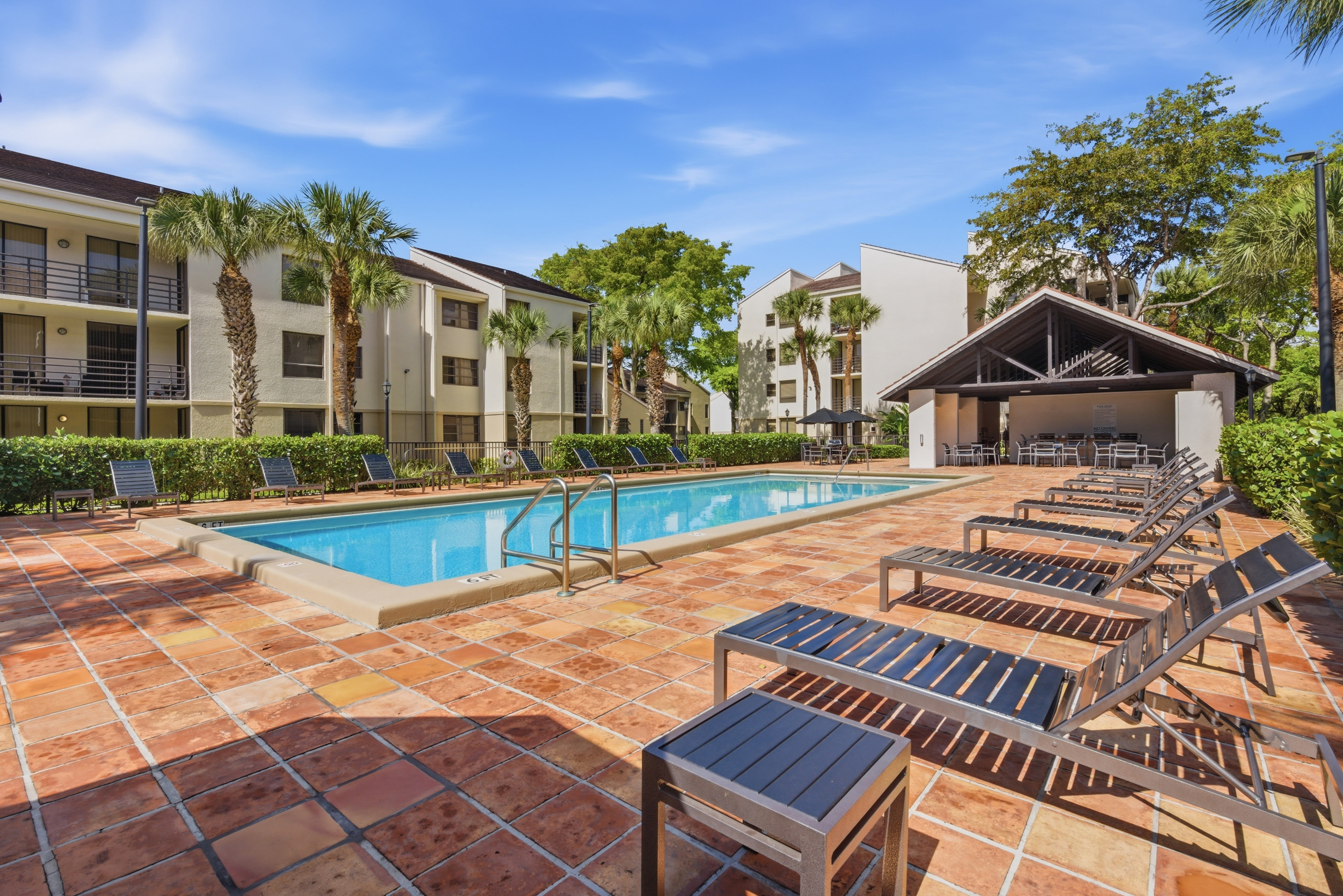 Resort-style swimming pool with plenty of lounge chairs and a poolside gazebo with barbecue grills at New Barn Apartments in Miami Lakes, Florida