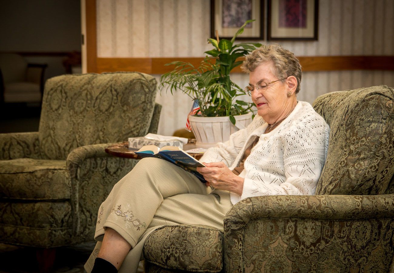 Resident sitting in a lounge chair reading a book at Villa at the Lake in Conneaut, Ohio
