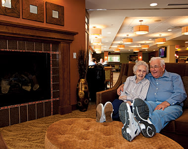 Resident couple at Clermont Park relaxing in front of the fireplace in one of the comfortable common areas