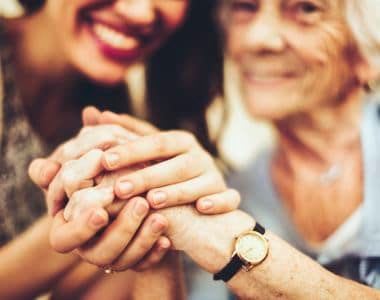Granddaughter and her grandmother smiling and holding hands at All American Assisted Living at Kingston