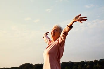Woman with her arms stretched out ot the sky in a field