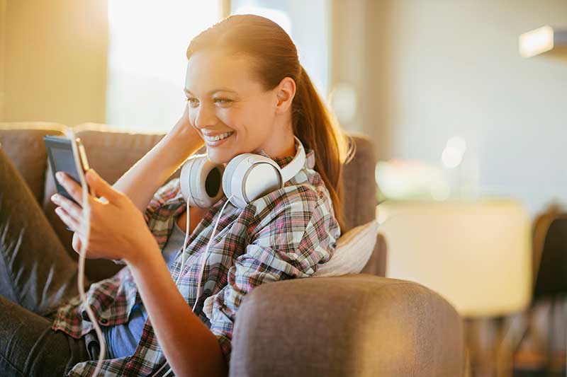 Smiling woman on couch looking at smart phone at The Landings Apartments in Clifton Park, New York