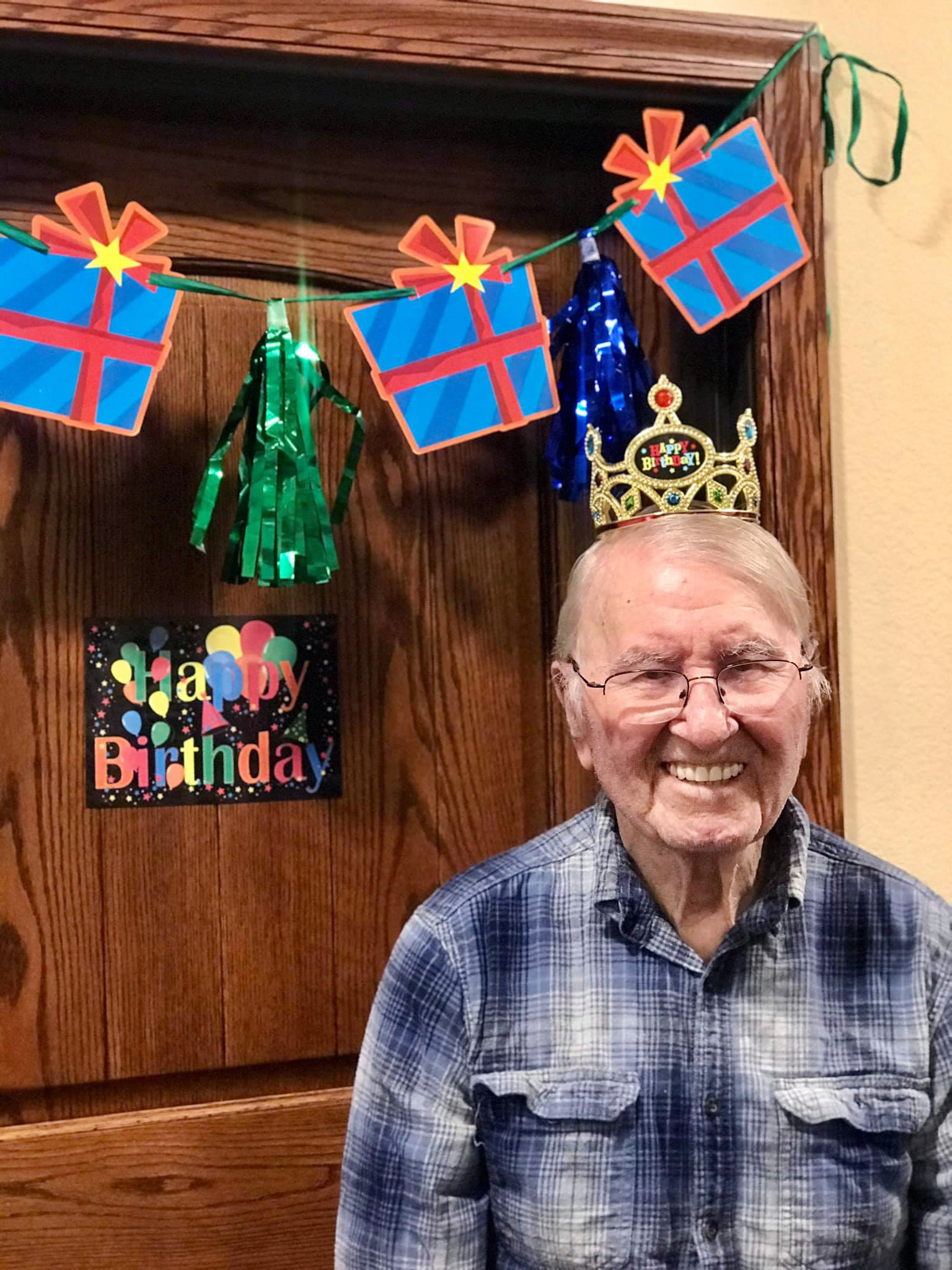 A resident smiling outside his apartment door, adorned with birthday decortations, at Oxford Glen Memory Care at Carrollton in Carrollton, Texas