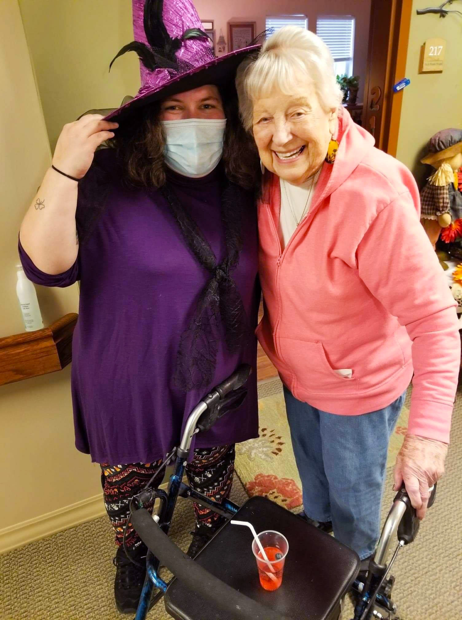 Masked caregiver in a witch costume side-hugging a resident at The Oxford Grand Assisted Living & Memory Care in Wichita, Kansas