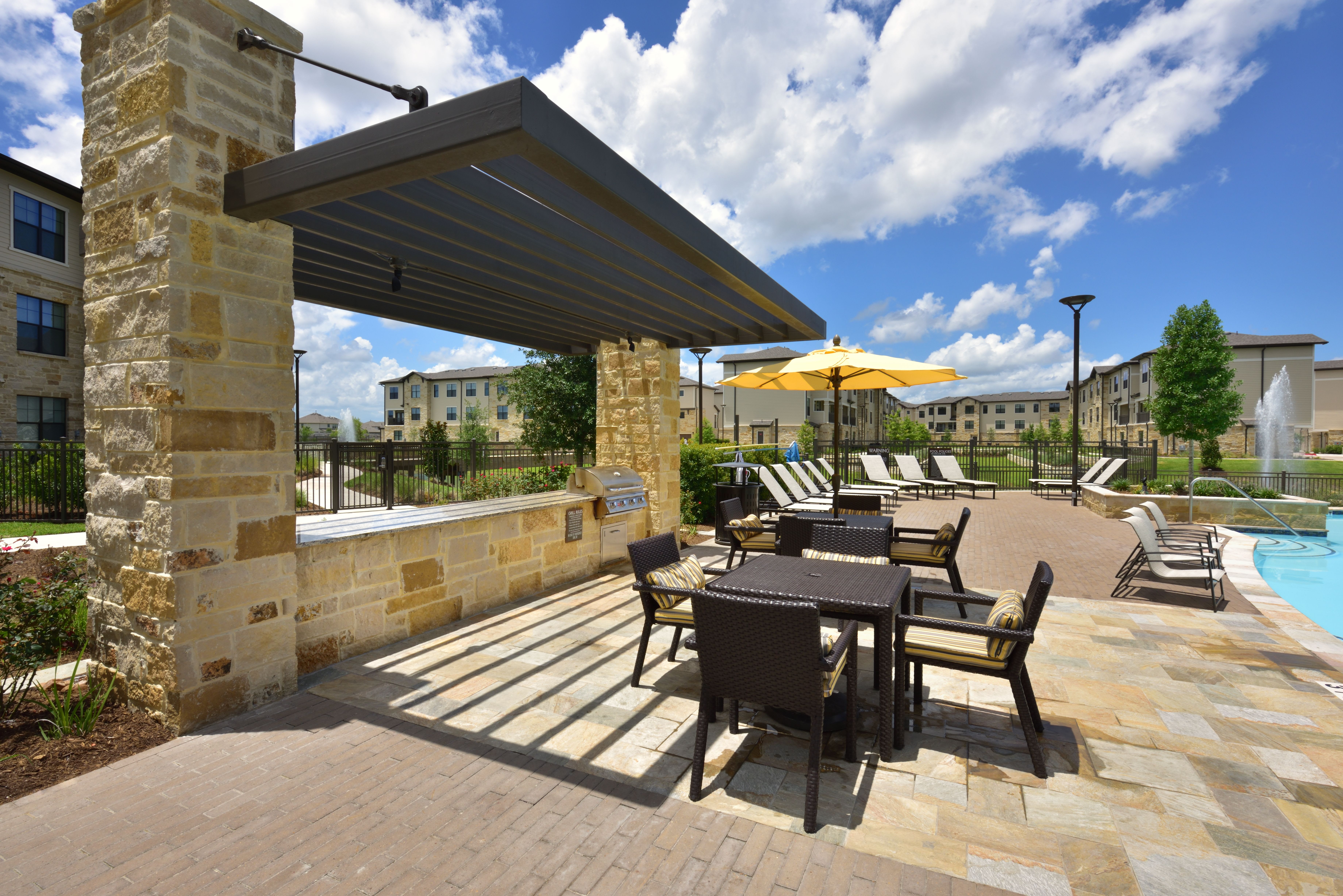 Stone BBQ with sitting tables and chairs on pool deck at Olympus Falcon Landing in Katy, TX