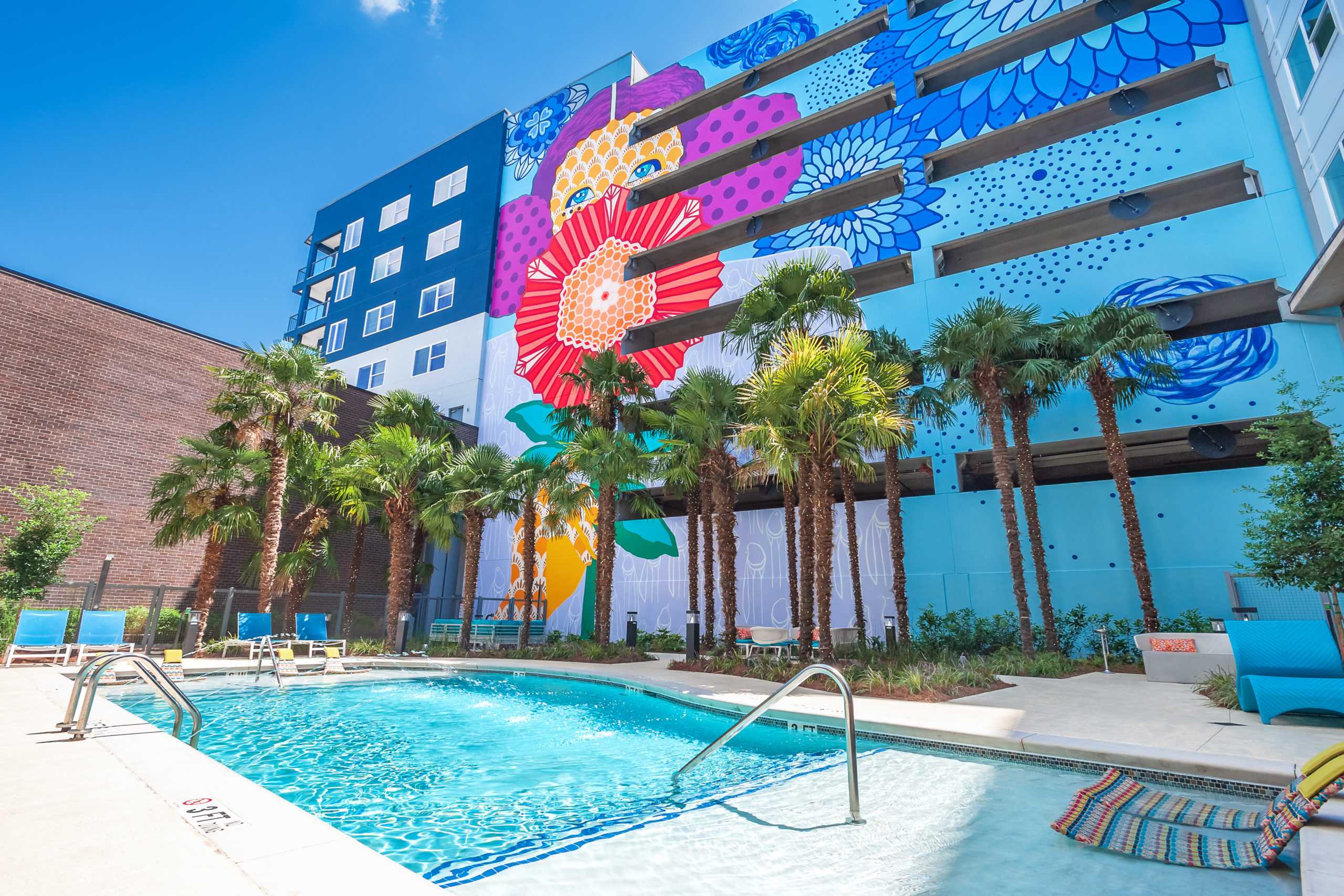 Heated resort-style swimming pool surrounded by palm trees and a vibrant mural at EDGE on the Beltline in Atlanta, Georgia