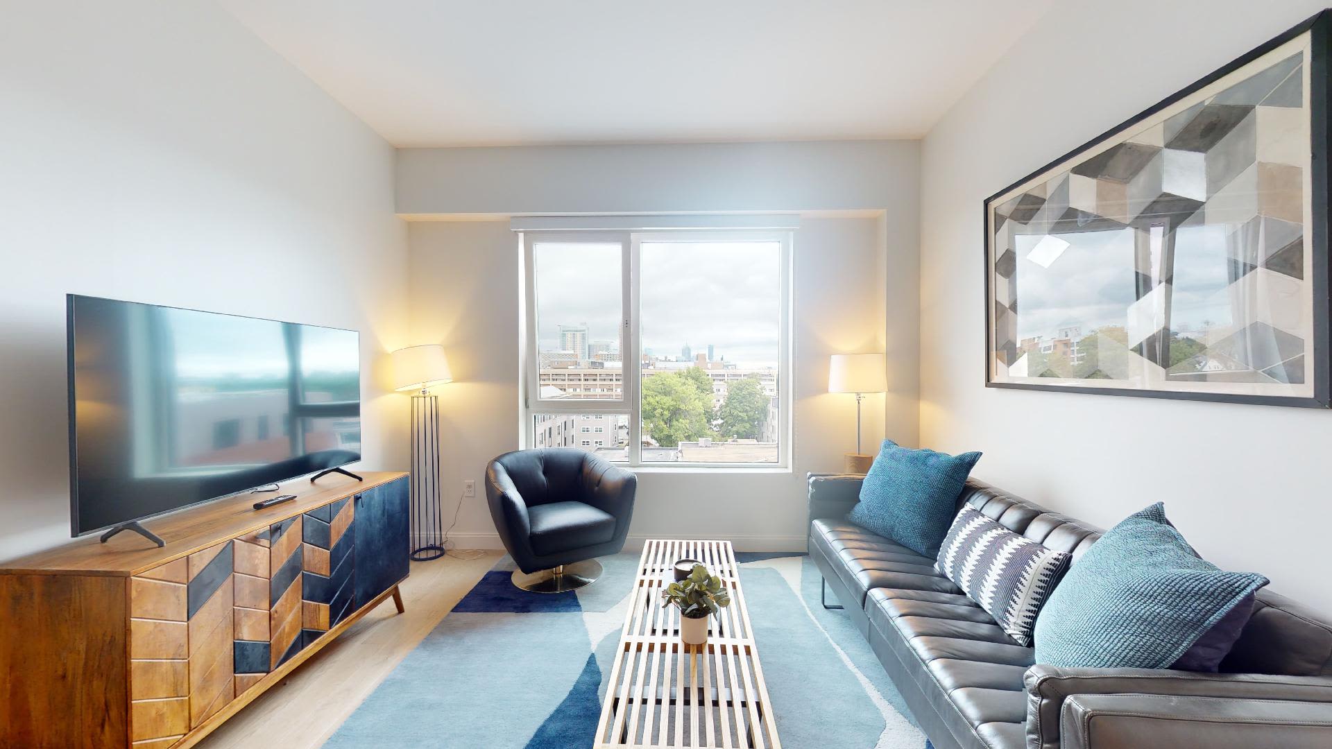 A furnished living room with a view of the city at 55 Brighton at Packard Crossing in Boston, Massachusetts