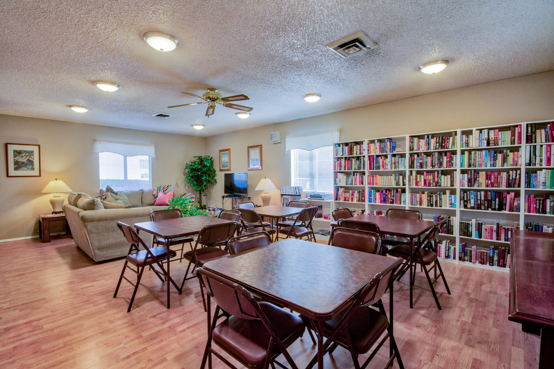 A club house with wooden tables, chairs, and bookshelves at Arbor Crest Apartments in Charlottesville, Virginia