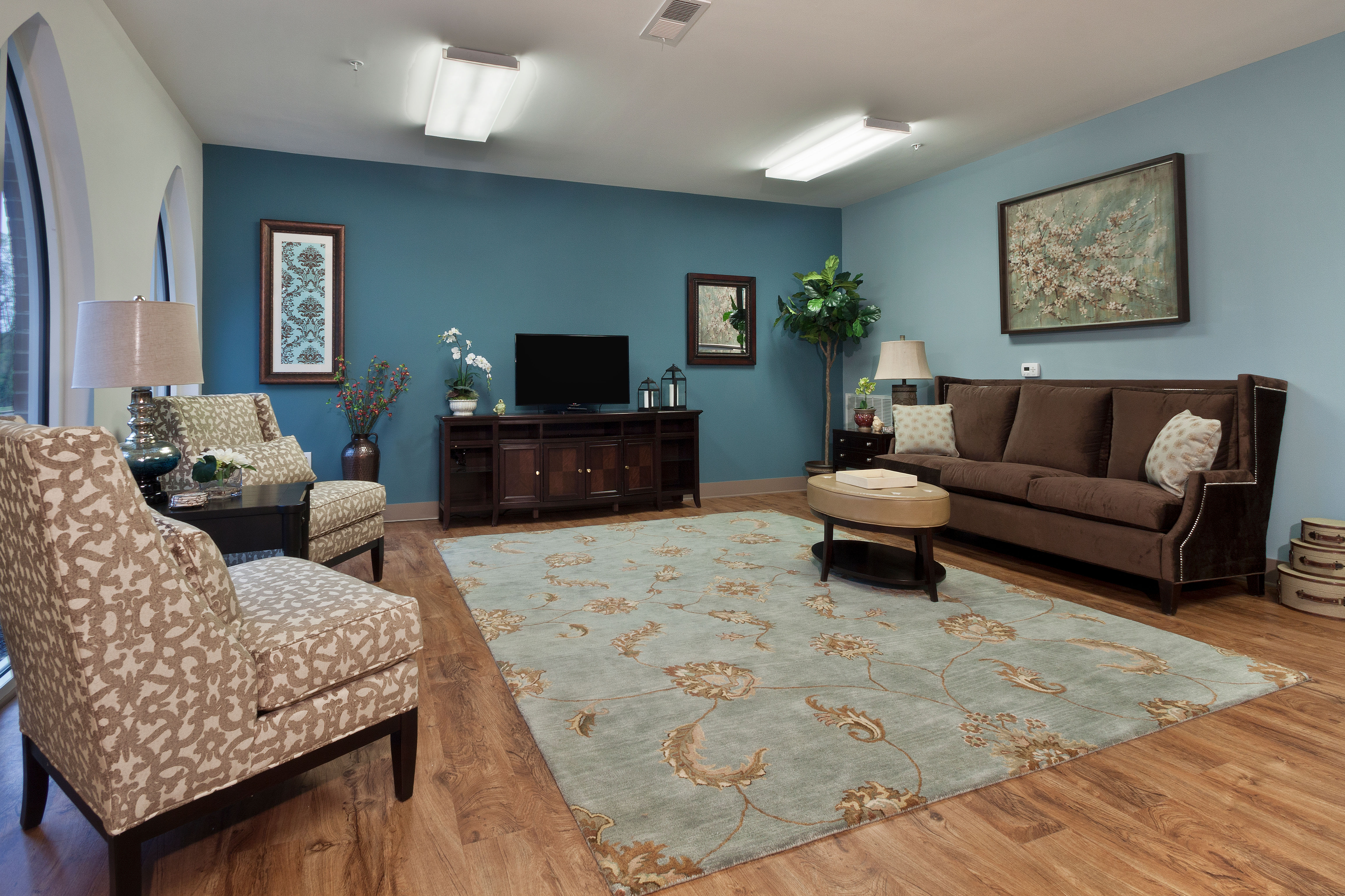Model living area with blue accents and wood flooring at Loftin II in Belmont, North Carolina