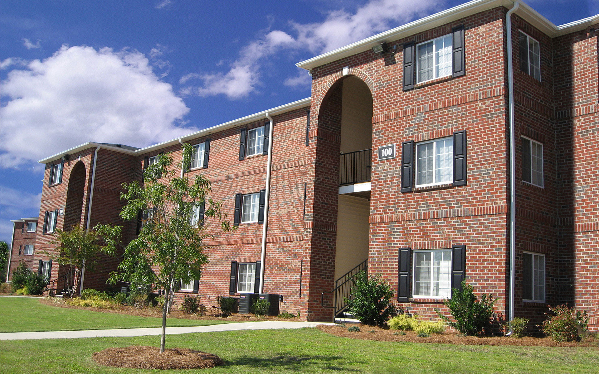 Brick building exterior with green grass and trees at Eagle Point Village in Fayetteville, North Carolina