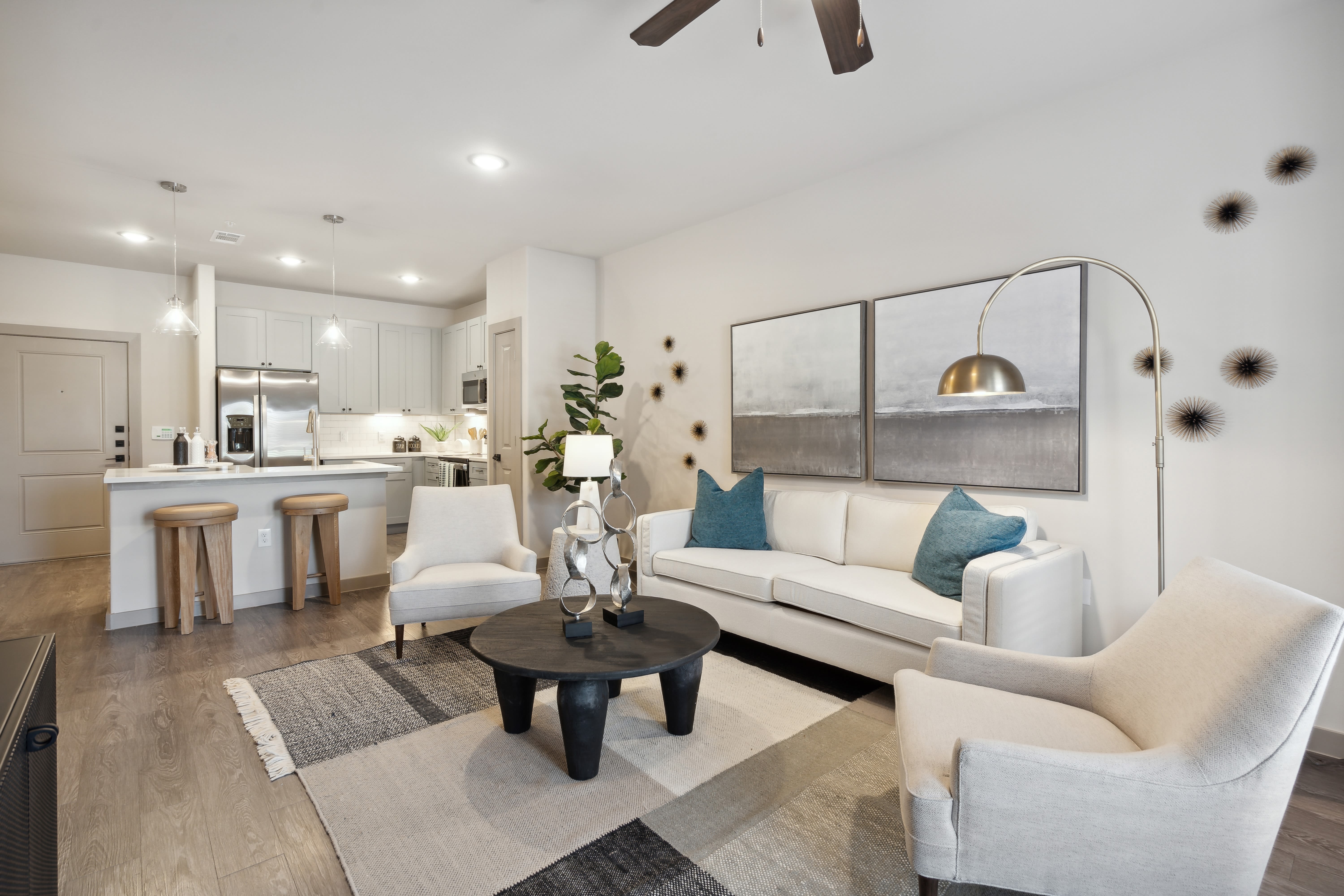 Living room and open kitchen of a beautifully decorated model apartment with wood-style plank flooring at Radius Wolf Ranch in Georgetown, Texas
