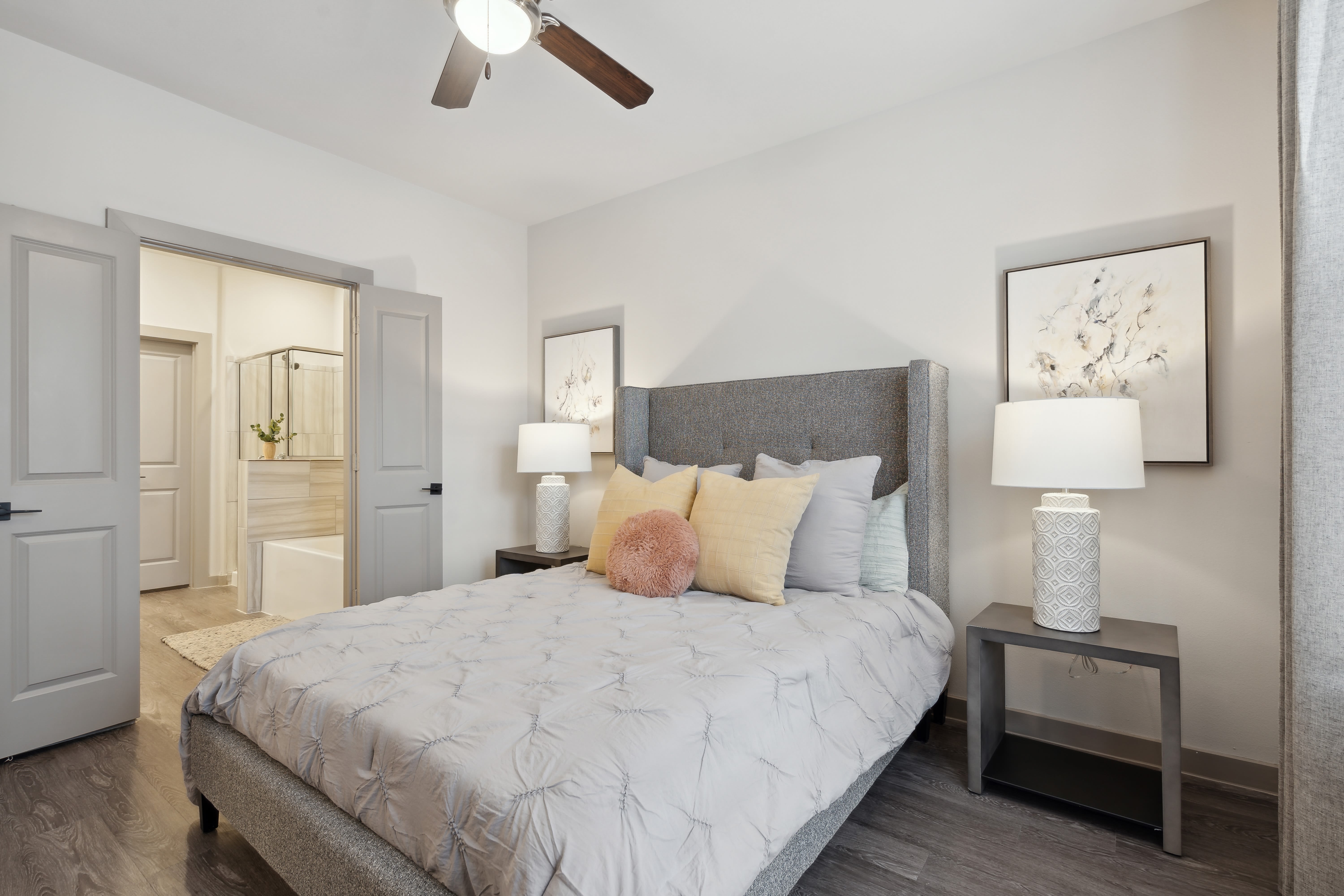 Model bedroom with attached bathroom and wood-style plank flooring at Radius Wolf Ranch in Georgetown, Texas