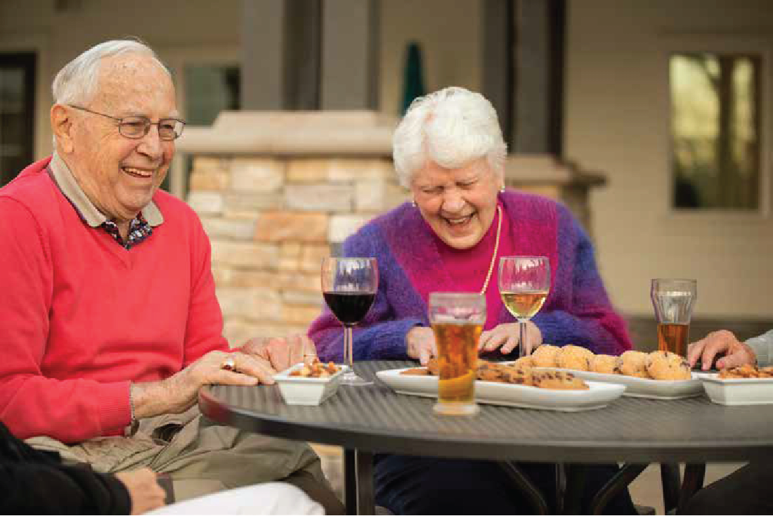 residents enjoying a meal and a laugh on an outdoor patio table at Clearwater at The Heights in Houston, Texas