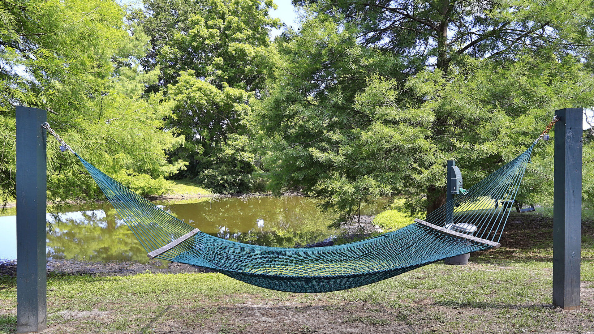 A green hammock suspended between poles, overlooking a pond and lush green trees at Thickett in Mt Pleasant, South Carolina