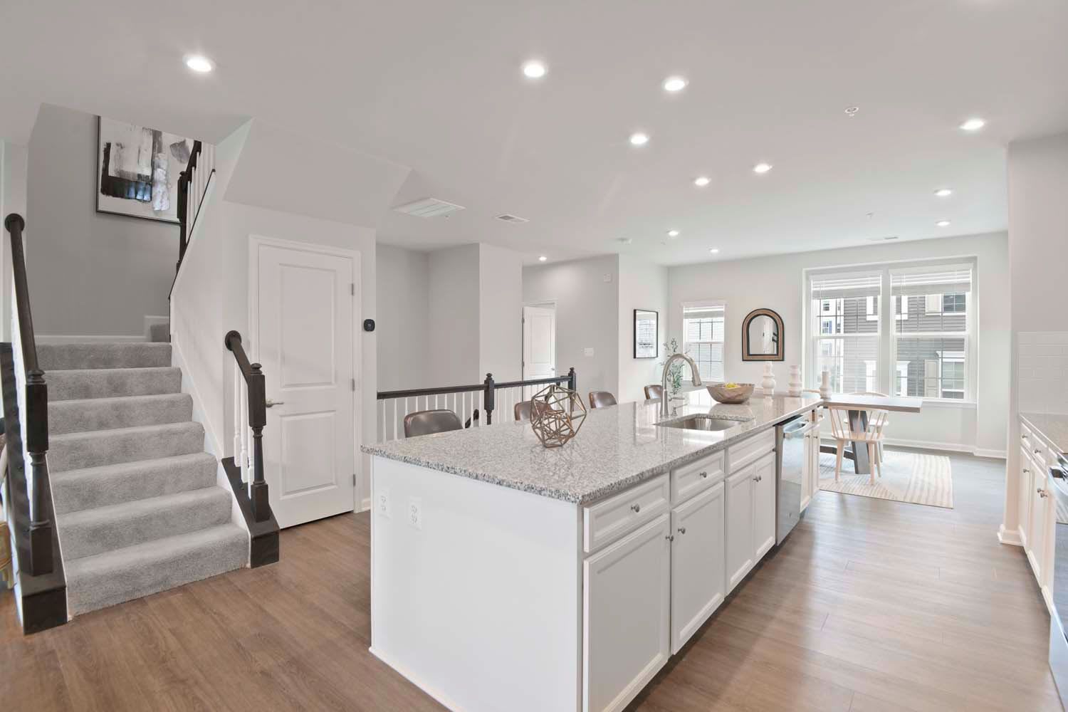 Open kitchen featuring a large granite island, white cabinetry, and a view of the dining area and stairs, creating a bright and functional space at Dorsey Overlook in Ellicott City, Maryland