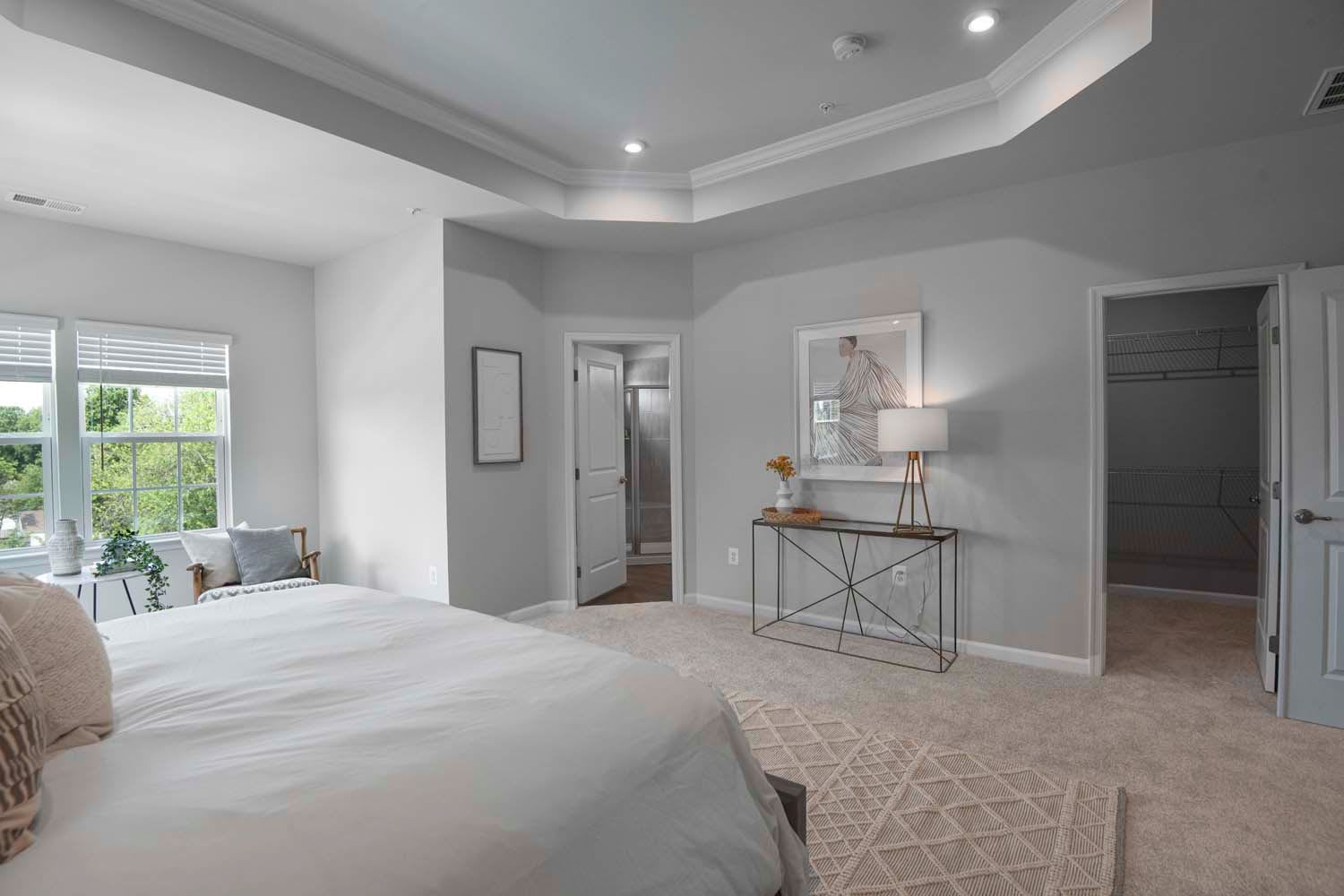 Elegant bedroom featuring a bed with soft linens, a stylish side table with a lamp, and an open doorway leading to a bathroom, complemented by a cozy area rug at Dorsey Overlook in Ellicott City, Maryland