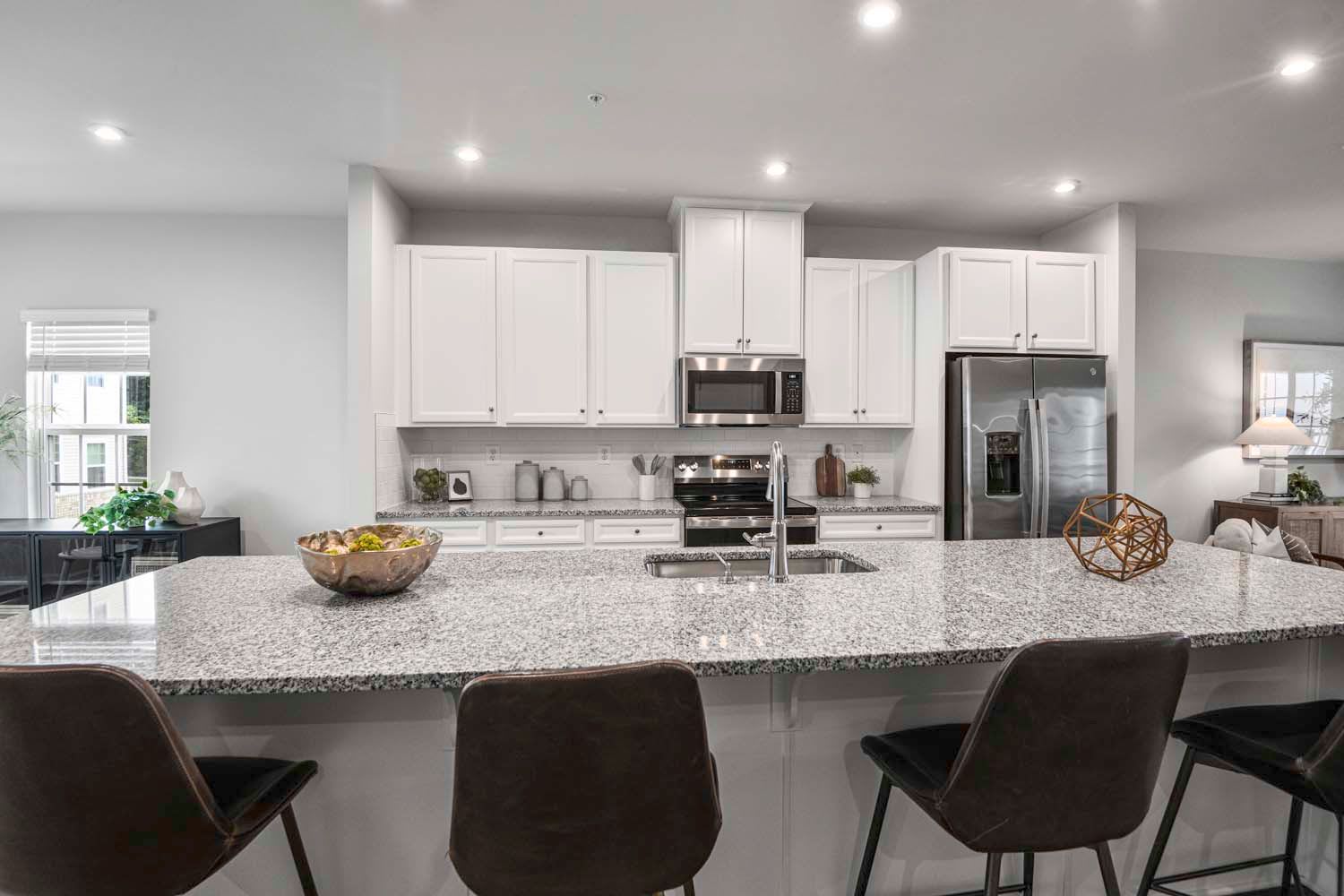 Modern kitchen with a large granite countertop, featuring a microwave and refrigerator, and stylish bar stools, creating a sleek and inviting space at Dorsey Overlook in Ellicott City, Maryland
