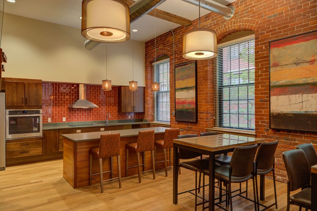 Fully-equipped open layout kitchen with stainless steel appliances and island with bar stools and pendant lights at The Lofts at 30 Pine in Gardner, Massachusetts