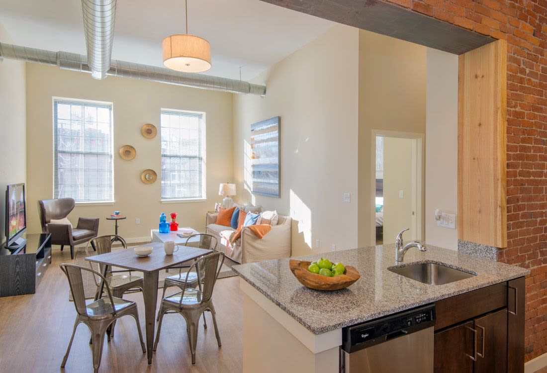 Open layout living room with hard-wood style flooring with dining table, couch, chair, TV, and windows view from kitchen island at The Lofts at 30 Pine in Gardner, Massachusetts