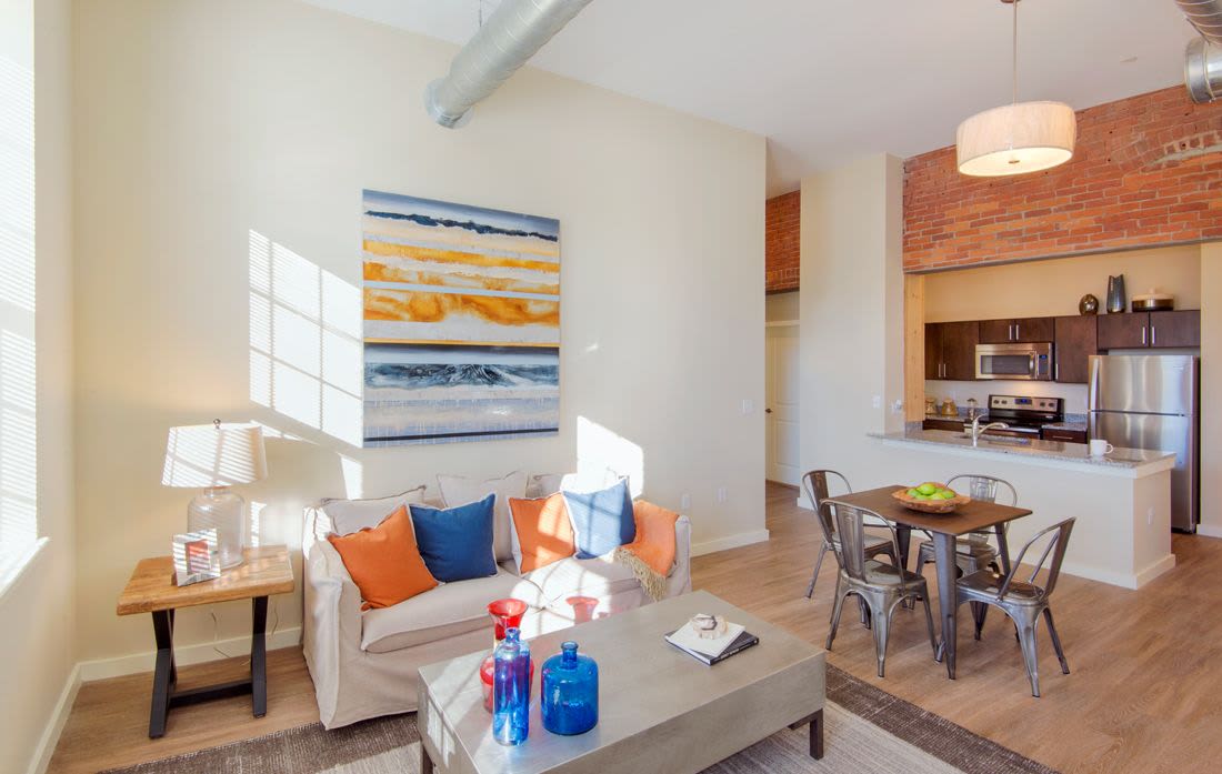 Open layout living room and connecting dining room kitchen with hard-wood style flooring and plenty of room for a couch and more at The Lofts at 30 Pine in Gardner, Massachusetts