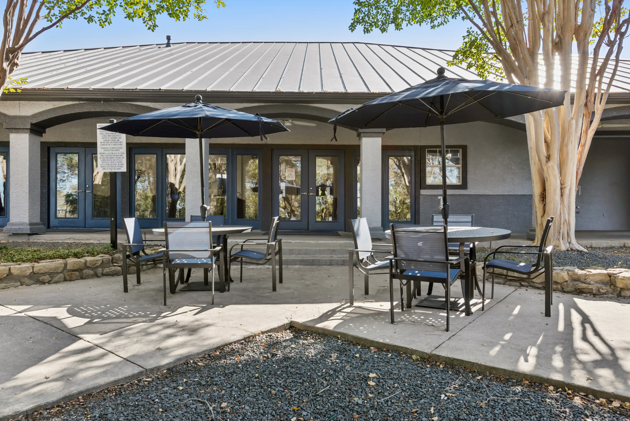 Outdoor patio area with round tables, black chairs, and large black umbrellas at Ellie Apartments in Austin, Texas