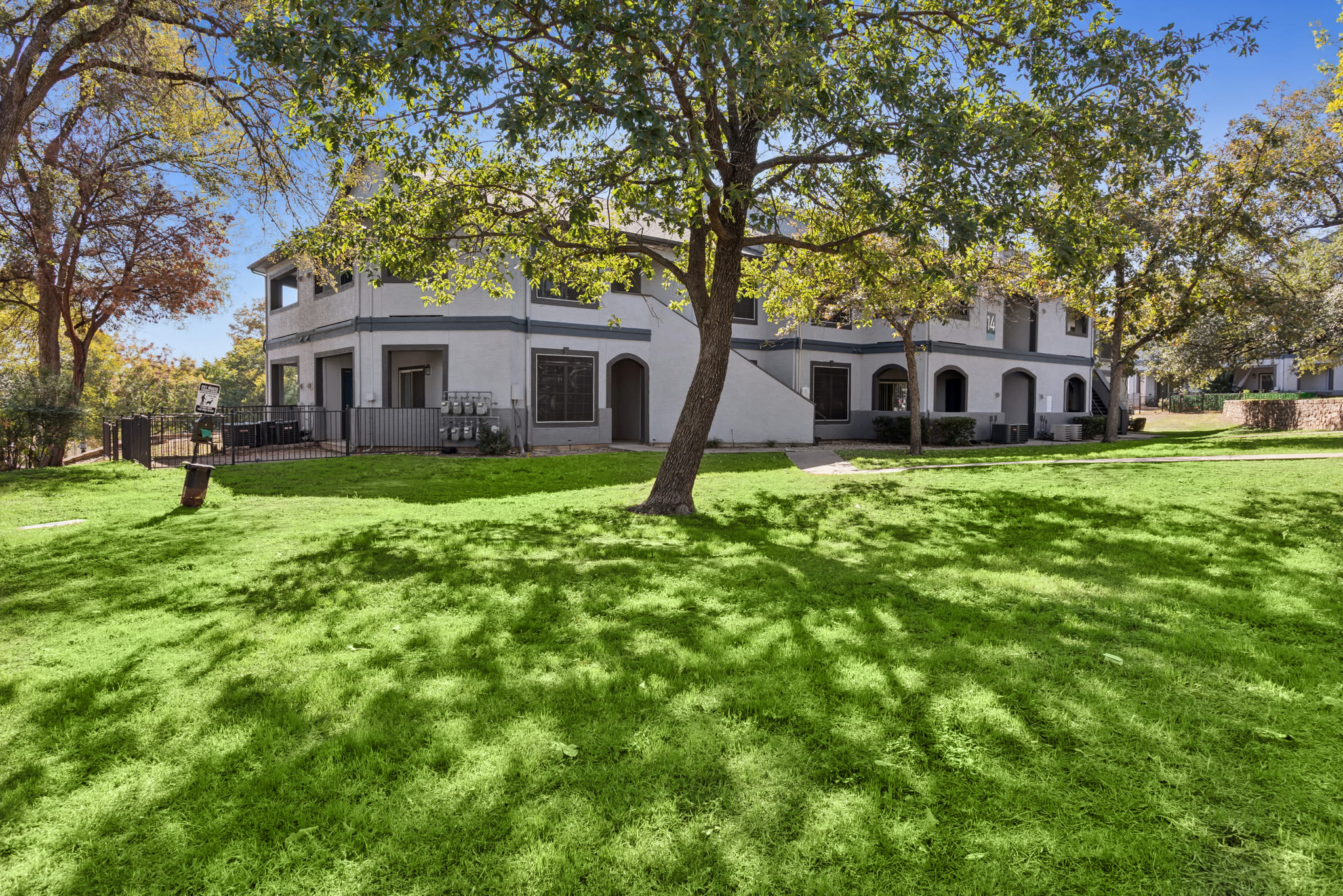 Two-story residential apartment buildings with light gray walls and dark trim, featuring argainst a sunny sky with a grassy lawn and trees at Ellie Apartments in Austin, Texas