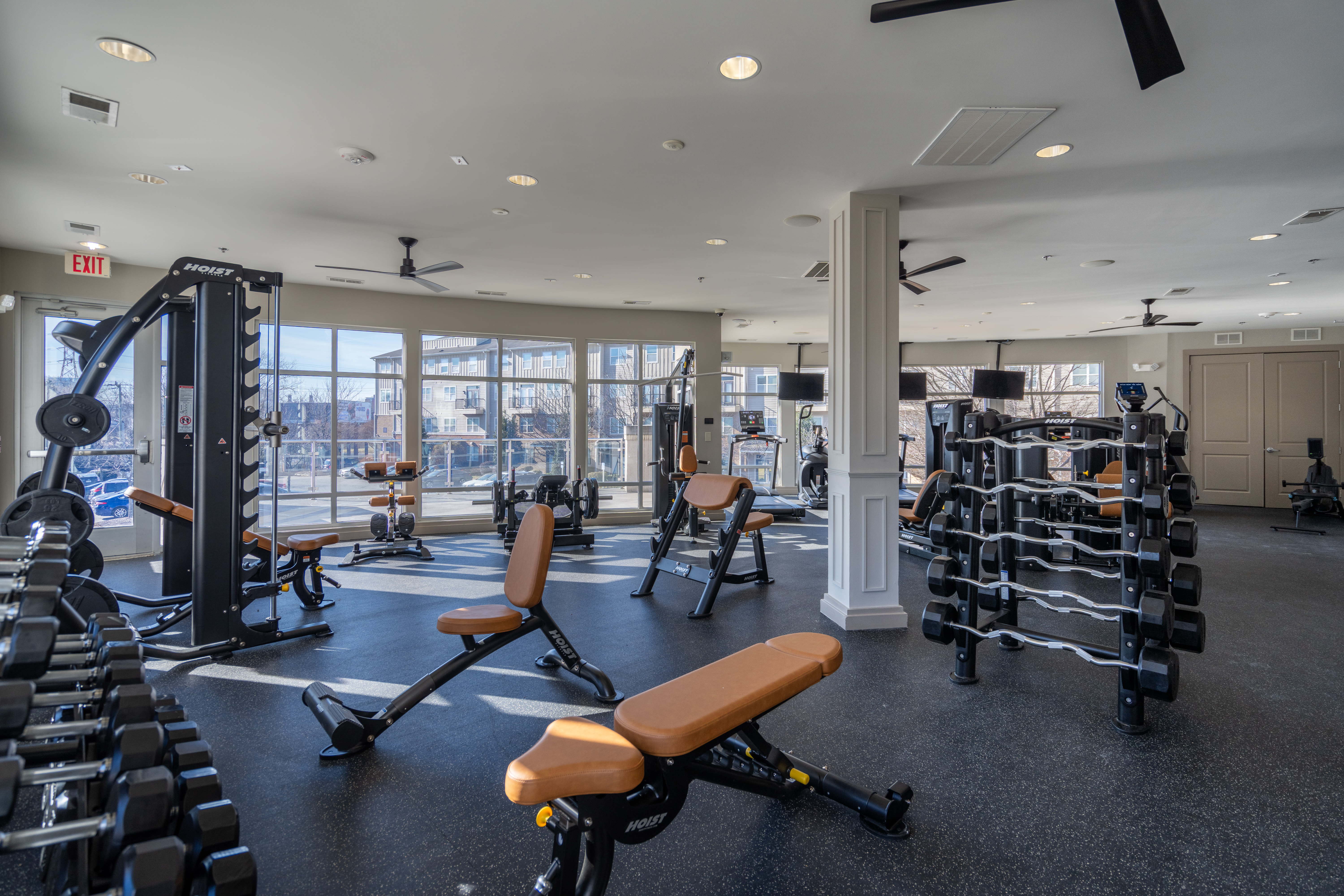 Fitness room with large floor‑to‑ceiling windows and various strength‑training machines, including benches, weight machines, and free weights at The James in Richmond, Virginia