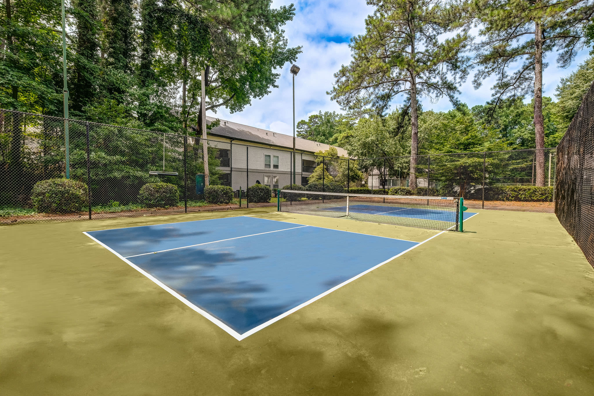 Outdoor tennis court surrounded by trees and fenced area near apartment buildings at LaVista Crossing in Tucker, Georgia