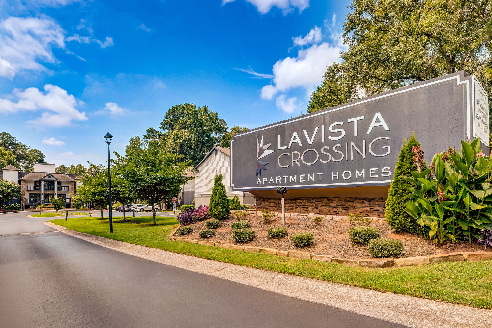 Exterior entrance sign for Lavista Crossing Apartment Homes with landscaping and clear skies at LaVista Crossing in Tucker, Georgia
