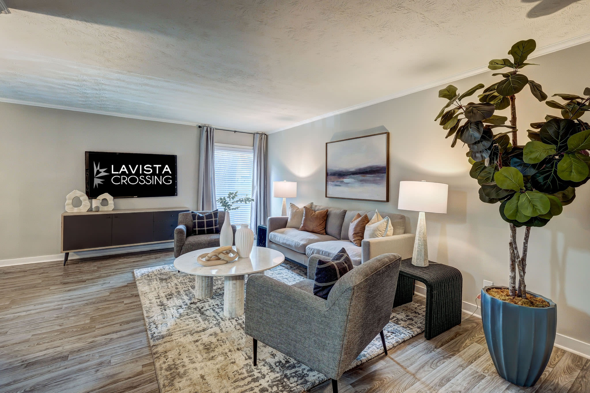 Modern living room with contemporary furniture, large indoor plant, artwork, and TV console at LaVista Crossing in Tucker, Georgia