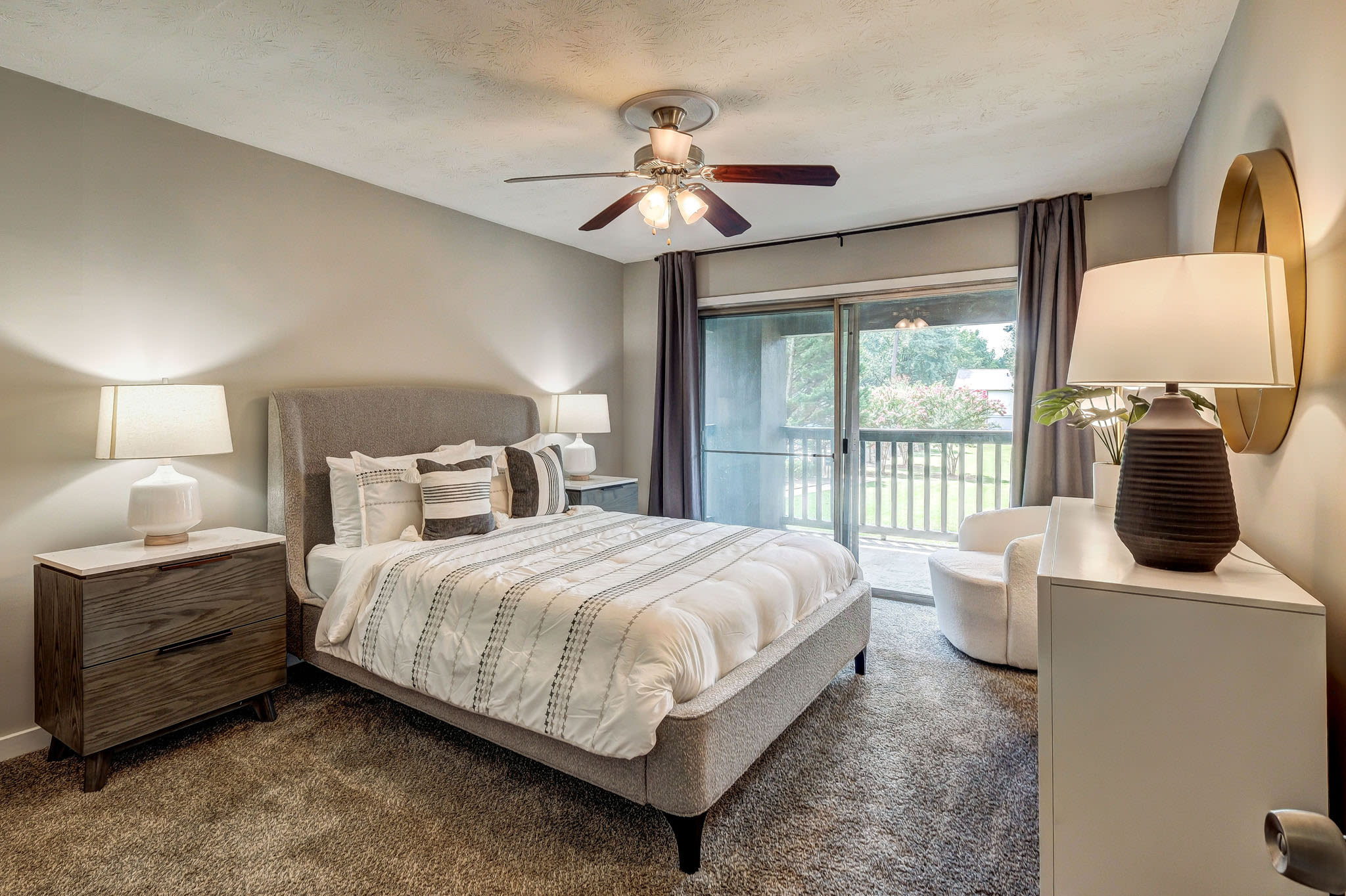 Cozy bedroom with carpet flooring, ceiling fan, large bed, and sliding door leading to balcony at LaVista Crossing in Tucker, Georgia