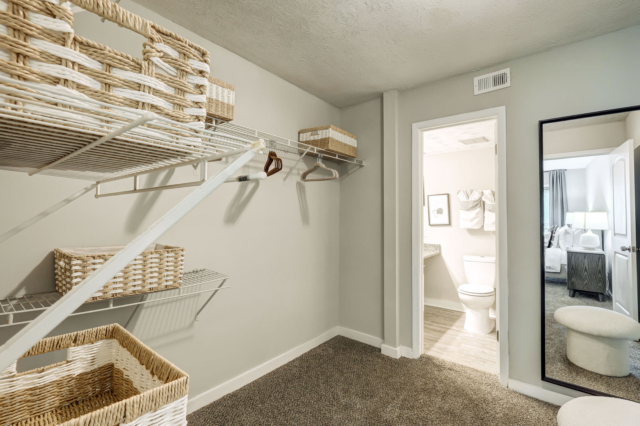 Walk‑in closet with shelving, wicker storage baskets, carpet flooring, and view into bathroom and bedroom at LaVista Crossing in Tucker, Georgia