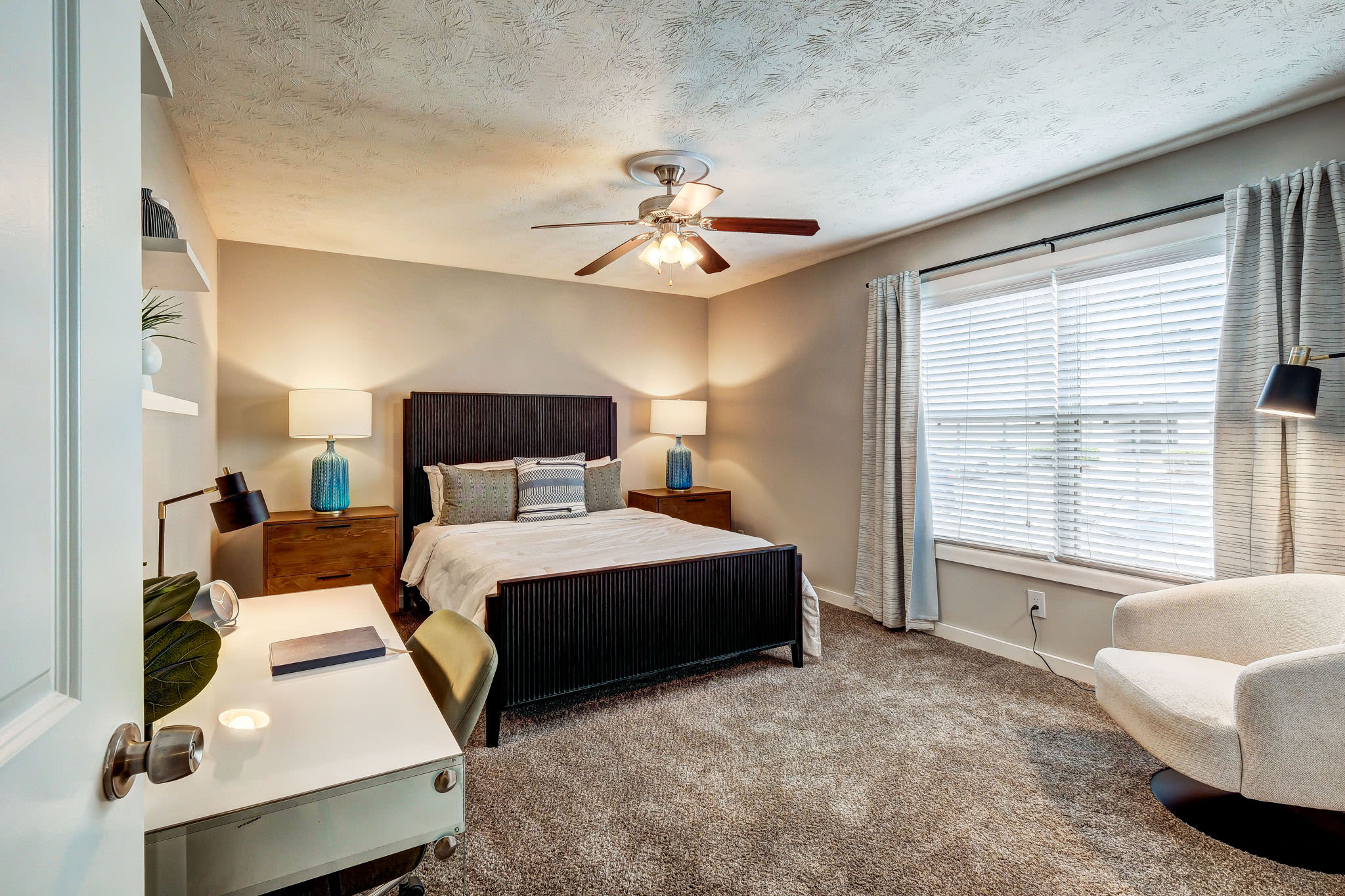 Bedroom with large window, modern bed, carpet flooring, and workspace desk at LaVista Crossing in Tucker, Georgia