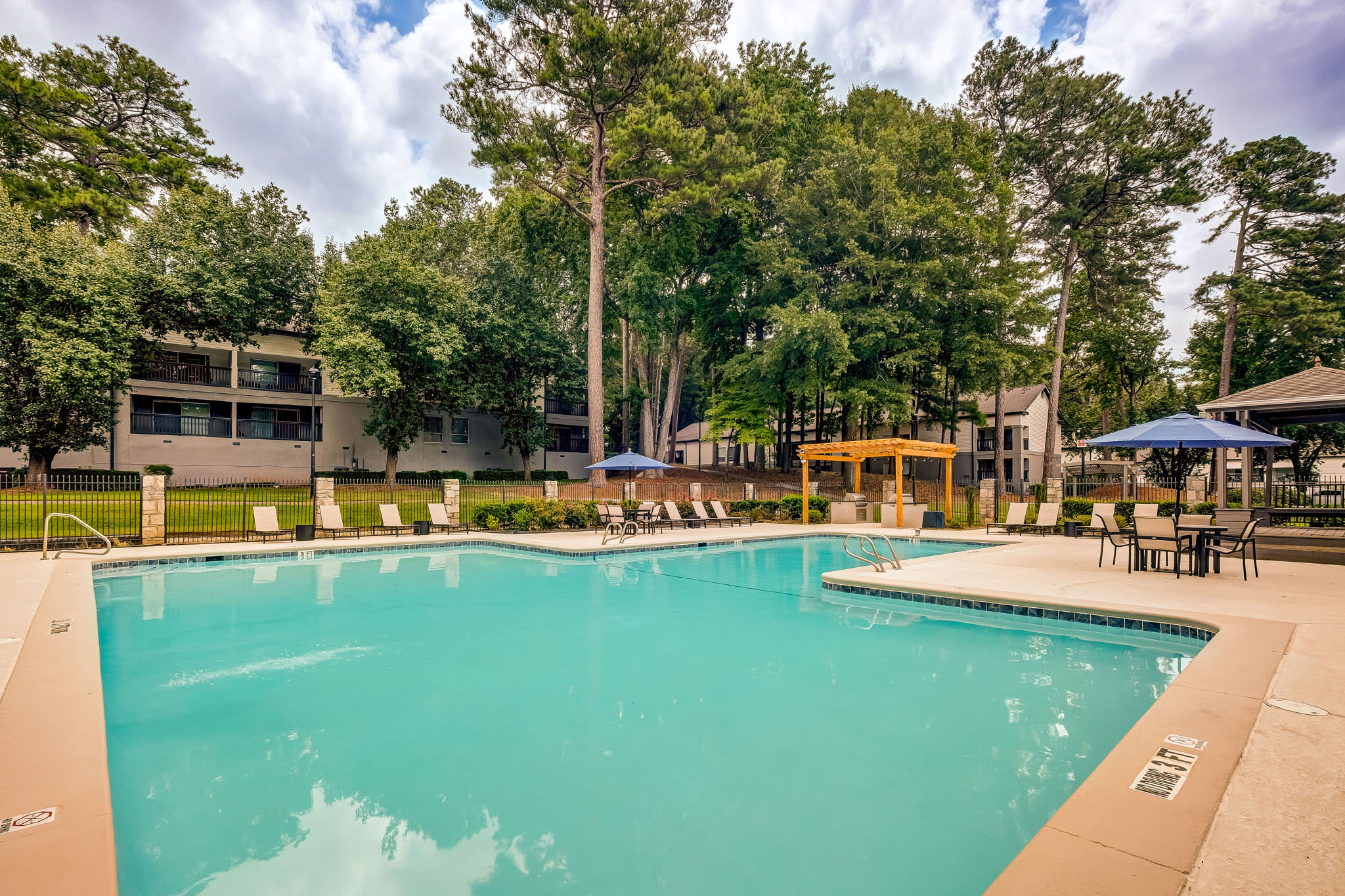 Large outdoor pool surrounded by trees, lounge seating, and shaded pergola areas at LaVista Crossing in Tucker, Georgia