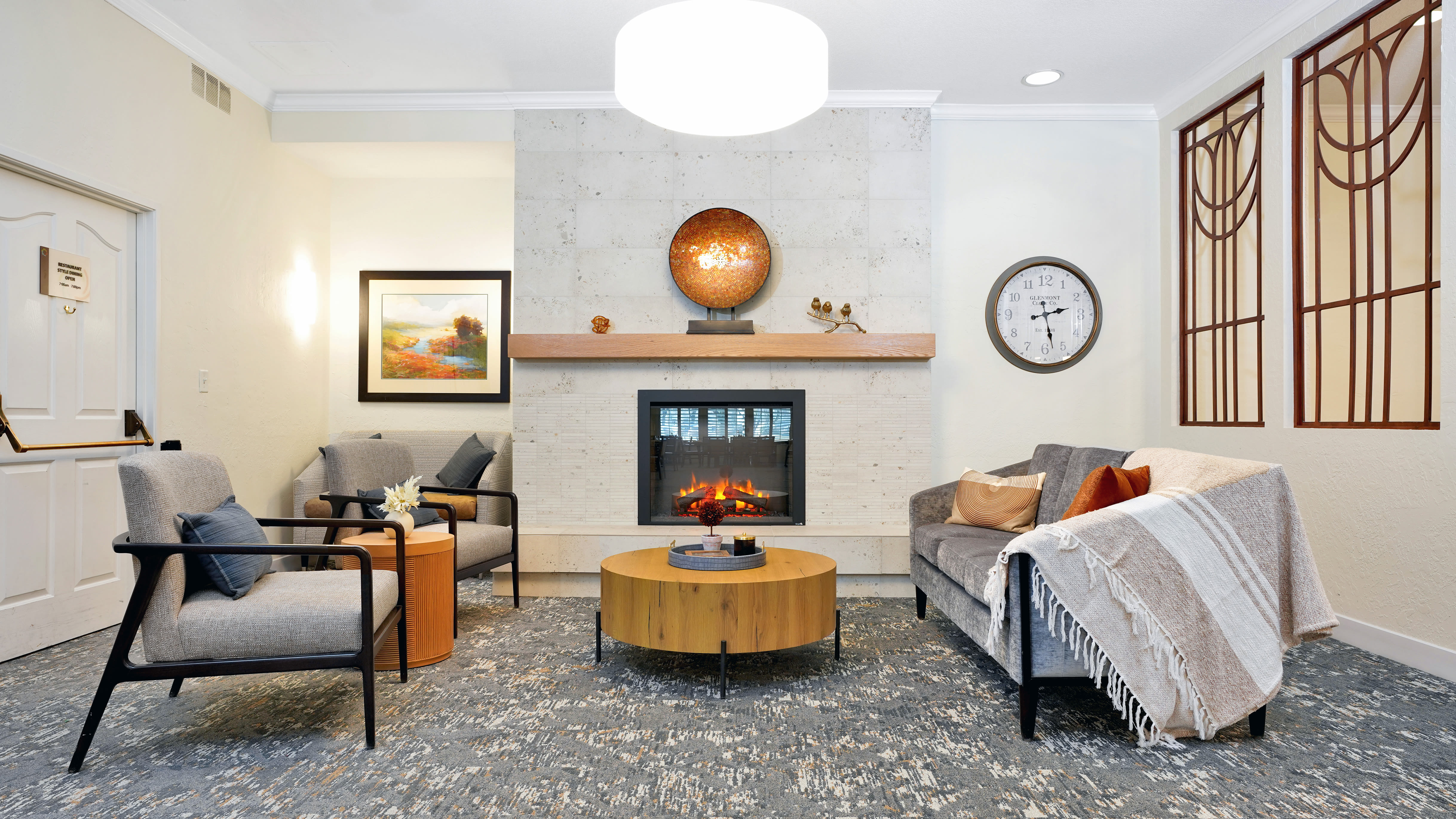 Cozy seating area with upholstered chairs, a sofa draped with a blanket, a modern fireplace, decorative wall art, and a round wooden coffee table at Cottonwood Creek in Salt Lake City, Utah.