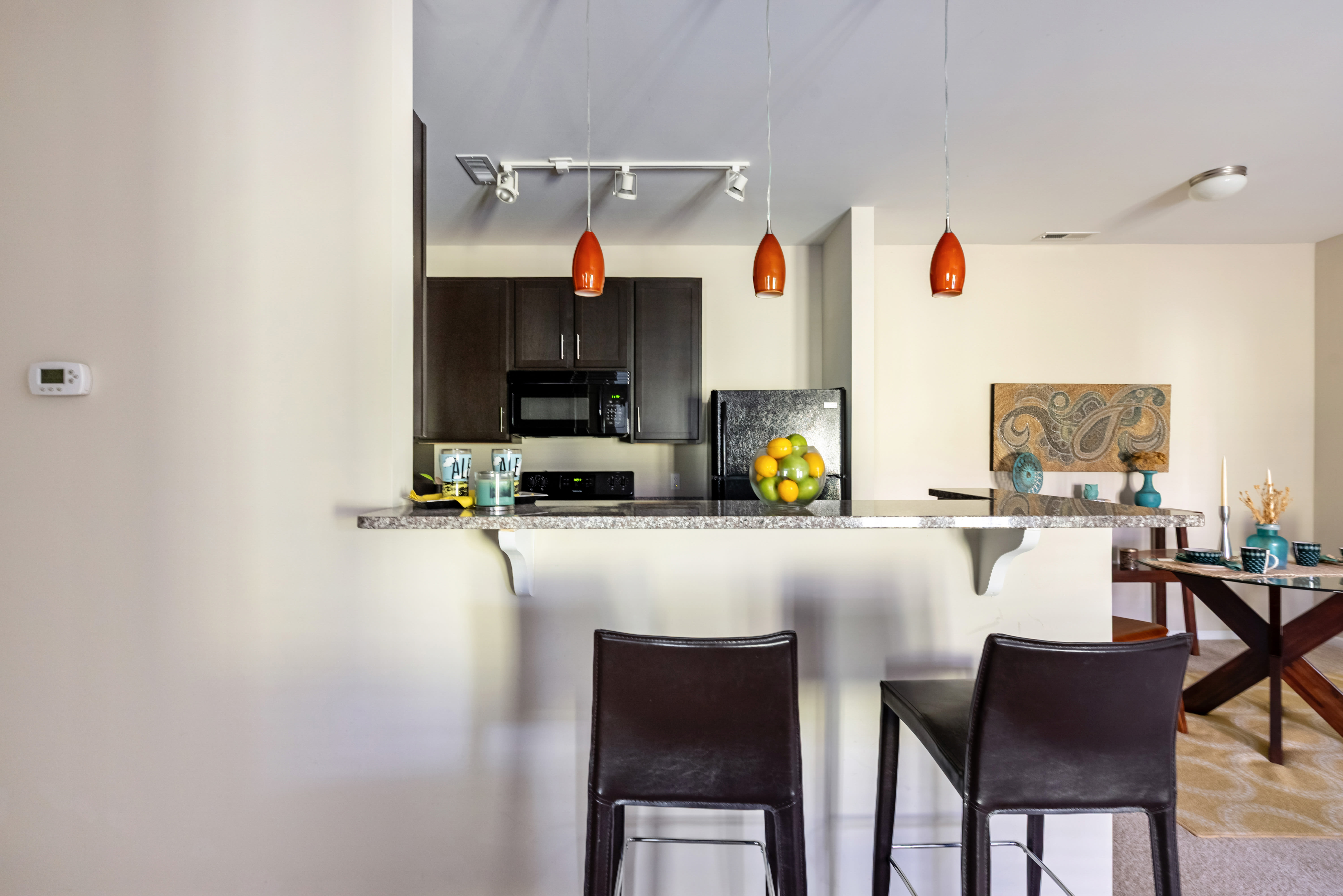 Kitchen with dark wood cabinets, granite countertops, black appliances, bar-height counter seating, and pendant lighting above the counter at Oak Grove Crossing Apartments in Newburgh, Indiana.