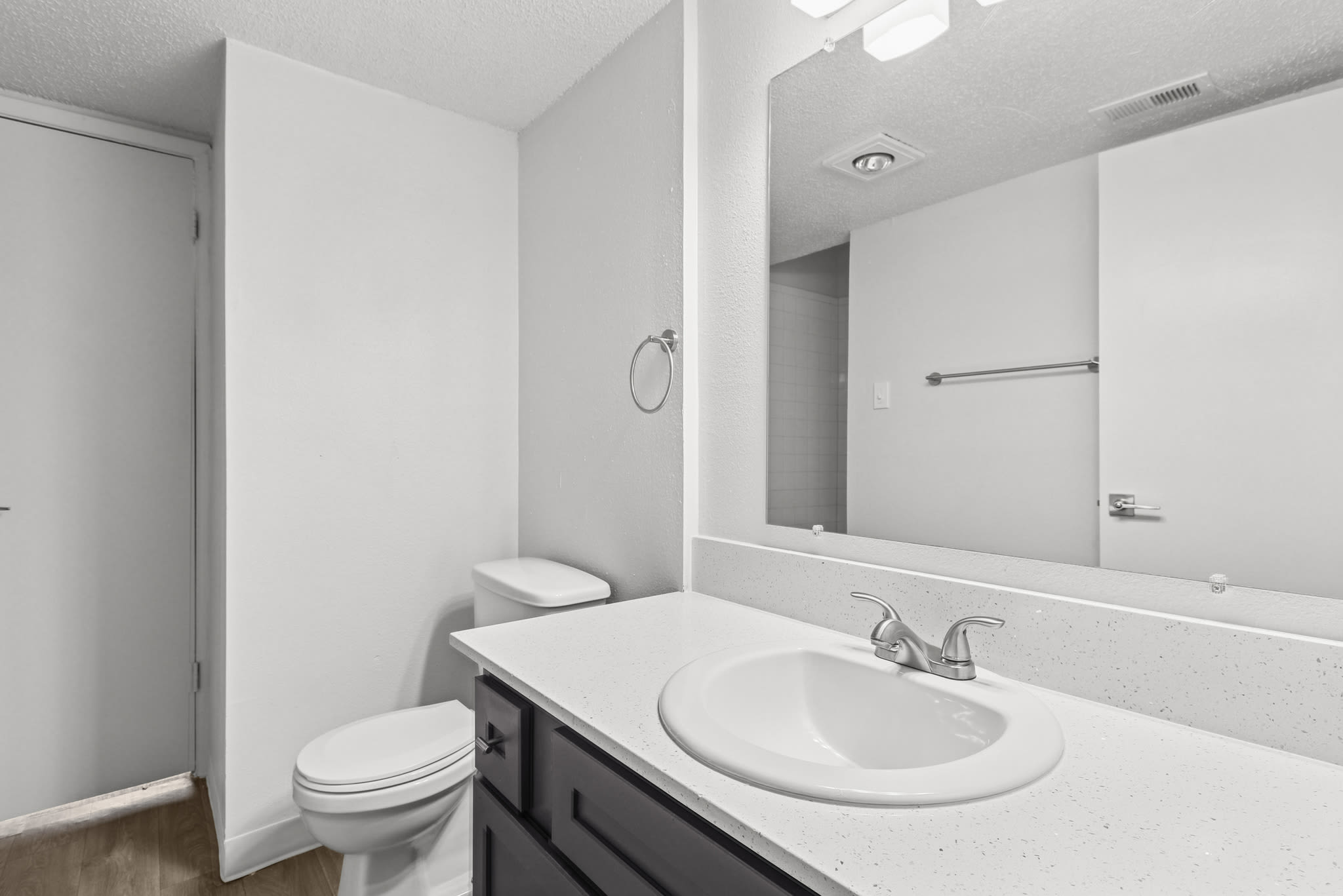 Bathroom with a single sink vanity, large mirror, and toilet against white walls at Pinewood Estates in Albuquerque, New Mexico