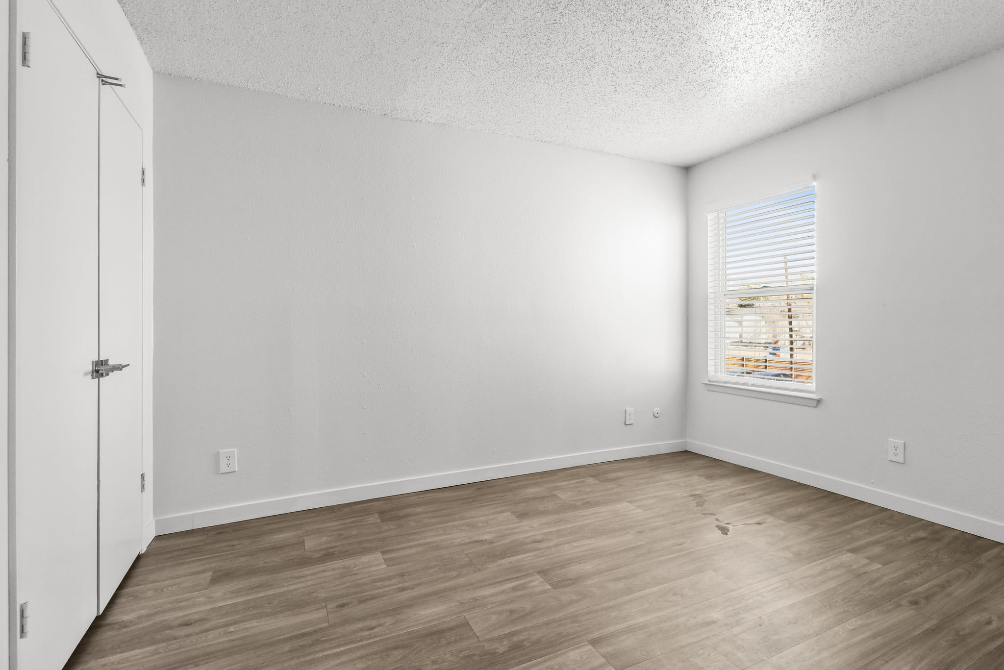 Bedroom with wood‑style flooring and a window letting in natural light at Pinewood Estates in Albuquerque, New Mexico