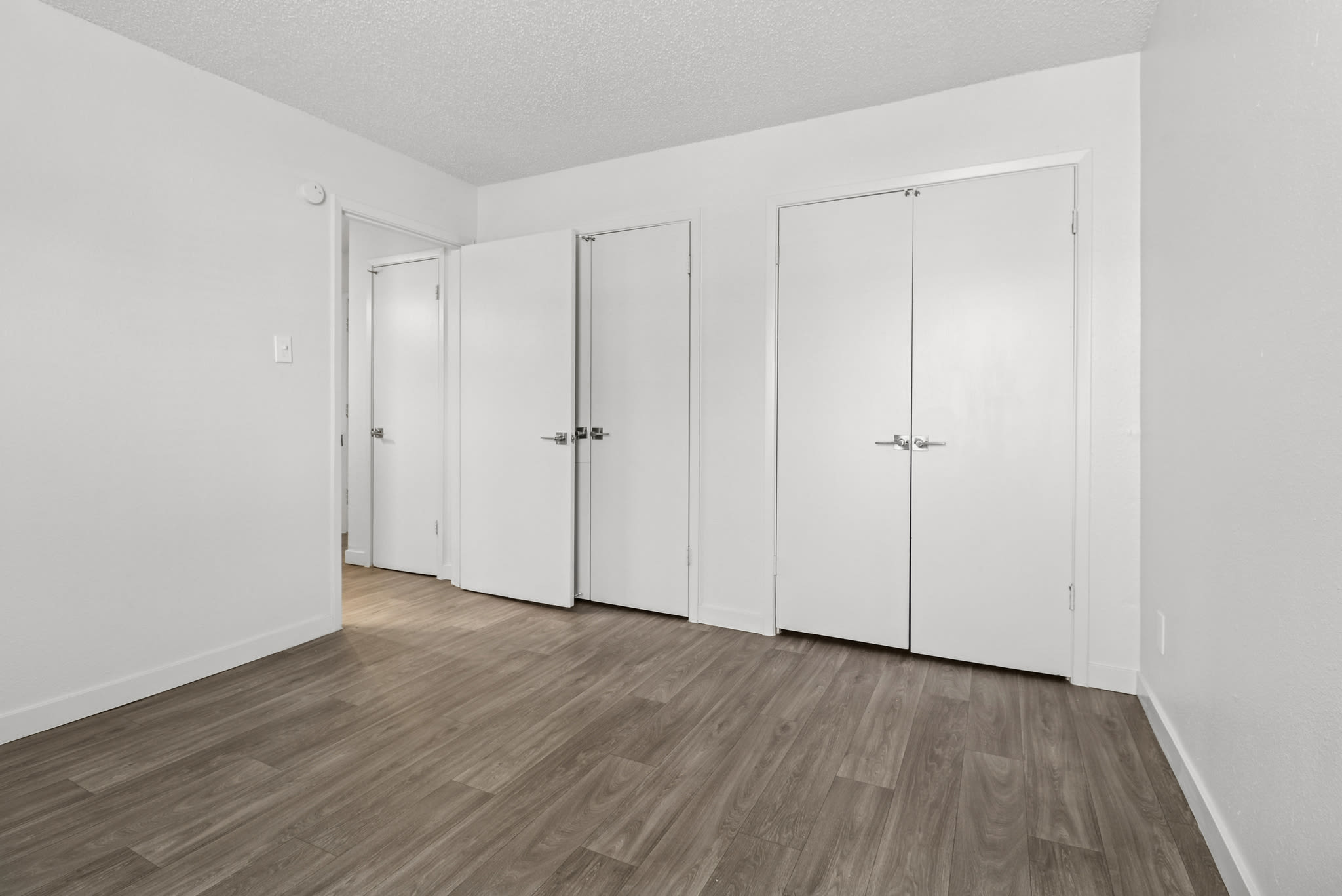 Empty bedroom with wood‑style flooring and several white doors at Pinewood Estates in Albuquerque, New Mexico