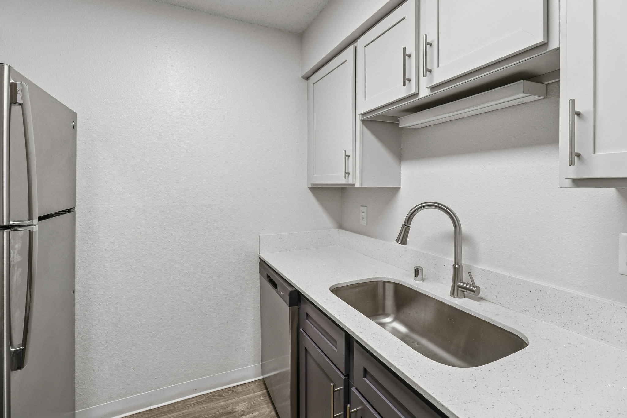 Kitchen with stainless steel sink, white cabinets, and wood‑style flooring at Pinewood Estates in Albuquerque, New Mexico