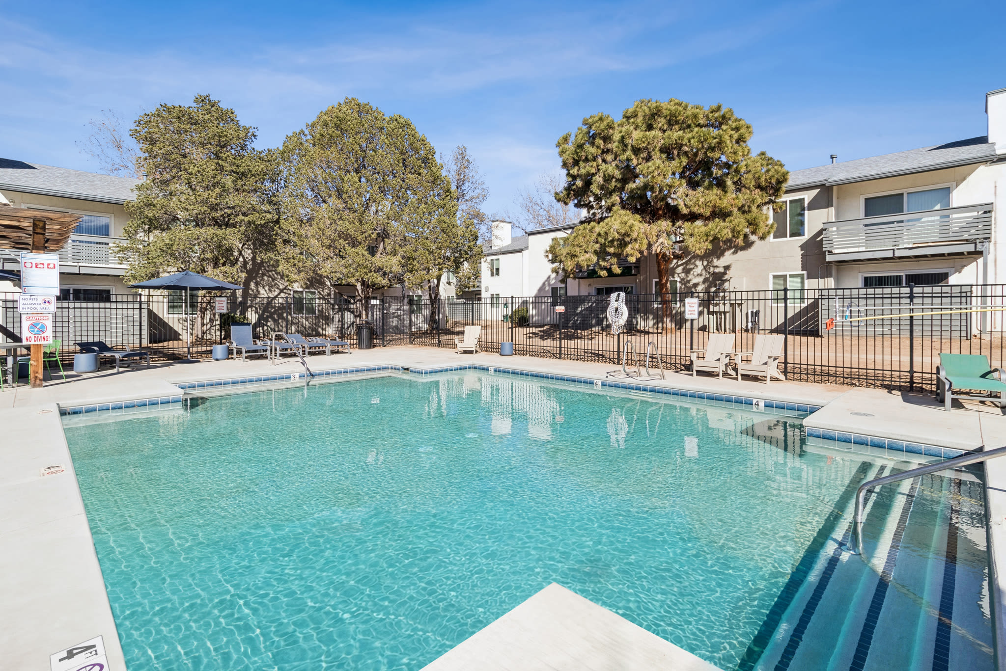 Outdoor pool surrounded by lounge chairs, fencing, and nearby apartment buildings at Pinewood Estates in Albuquerque, New Mexico