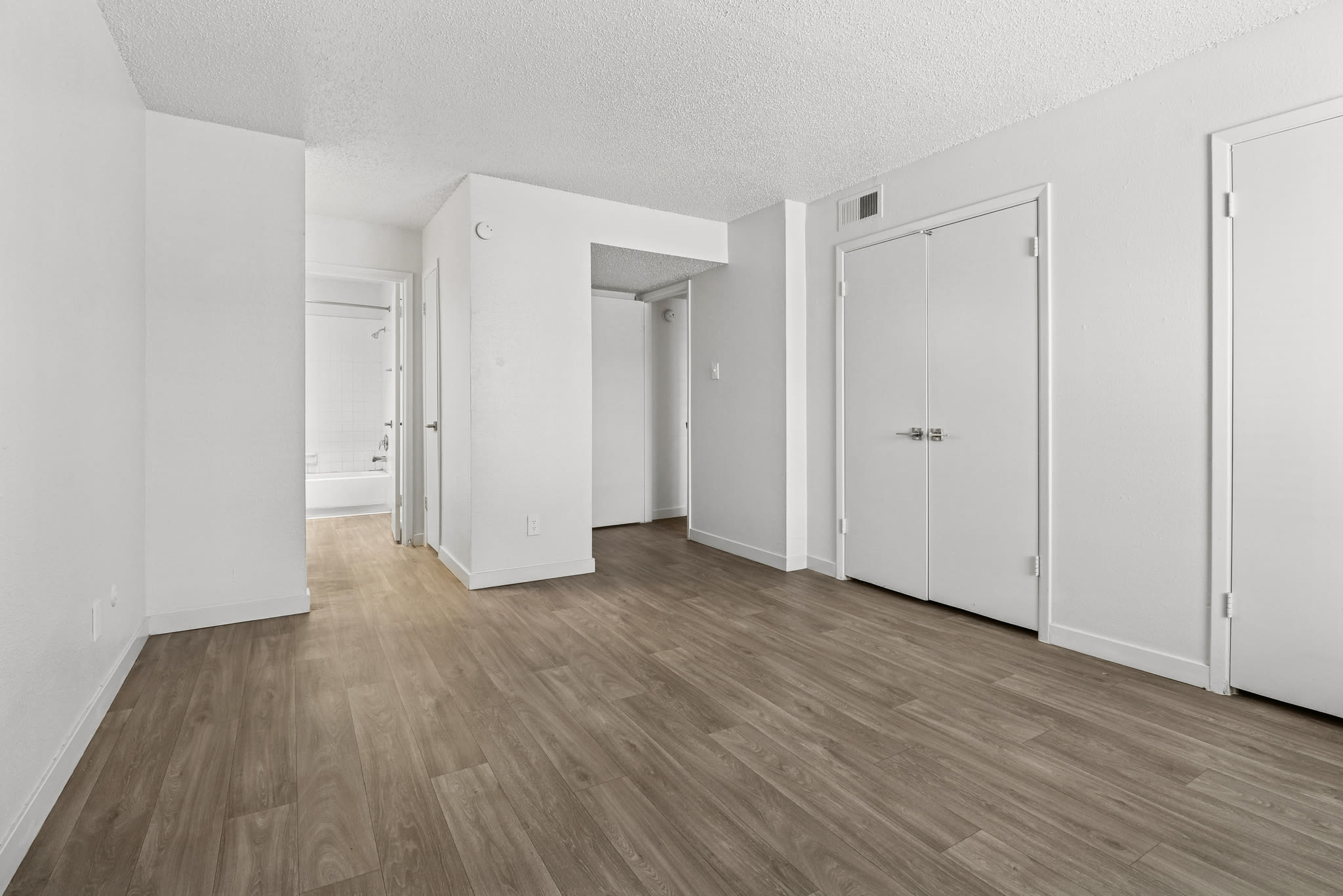 Empty room with wood‑style flooring and doorway leading to bathroom at Pinewood Estates in Albuquerque, New Mexico
