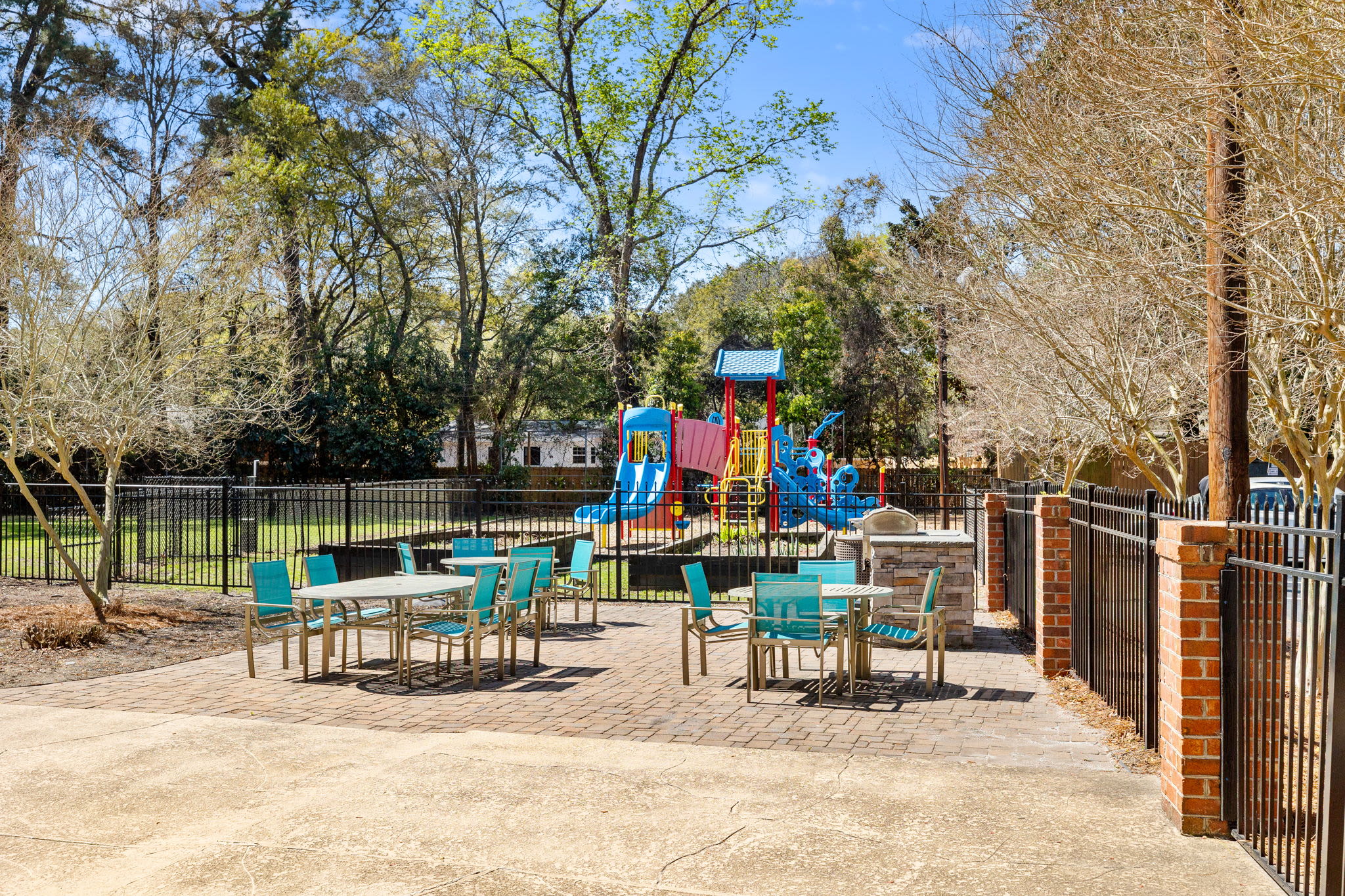 Outdoor patio with tables and chairs beside a fenced playground with colorful play structures at Palmetto Square in Charleston, South Carolina