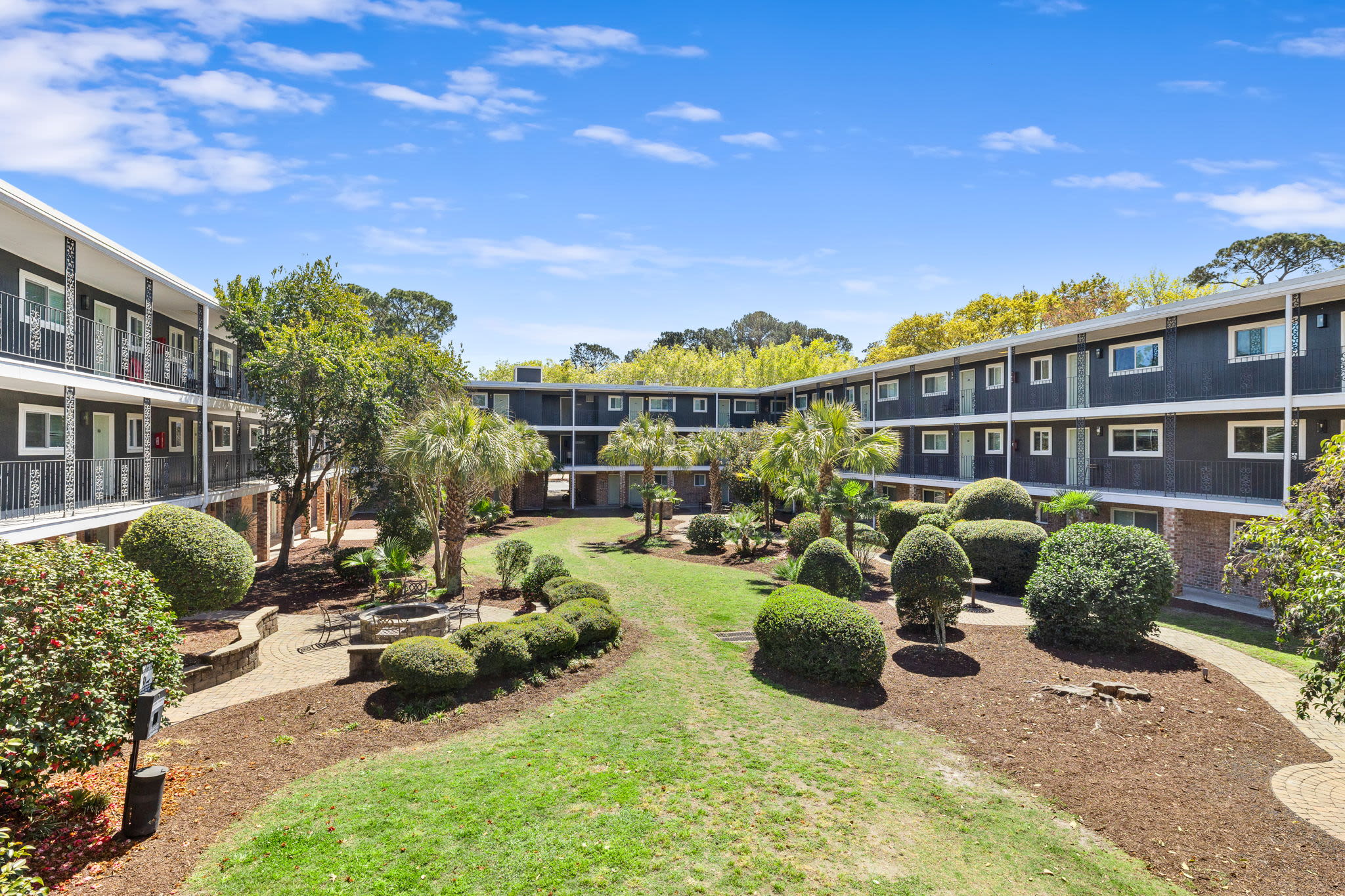 Apartment courtyard with circular fire pit, outdoor chairs, paved seating area, and surrounding residential buildings at Palmetto Square in Charleston, South Carolina