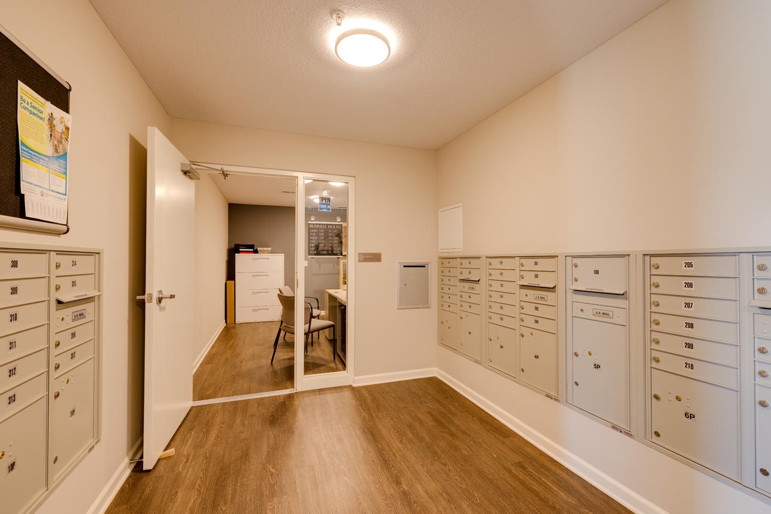 Bright hallway with mailboxes and a glass door leading to a business center with chairs at Johnston Crossing I in Johnston, Iowa